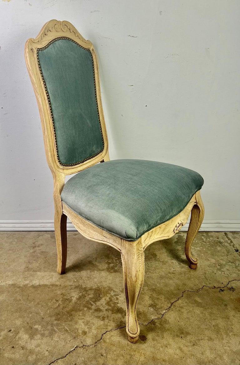 Set of eight painted French Louis XV style dining chairs newly upholstered in blue velvet and finished with a row of nailheads. The chairs stand on cabriole legs that end in rams head feet. There are an opposing pair of acanthus leaves depicted at
