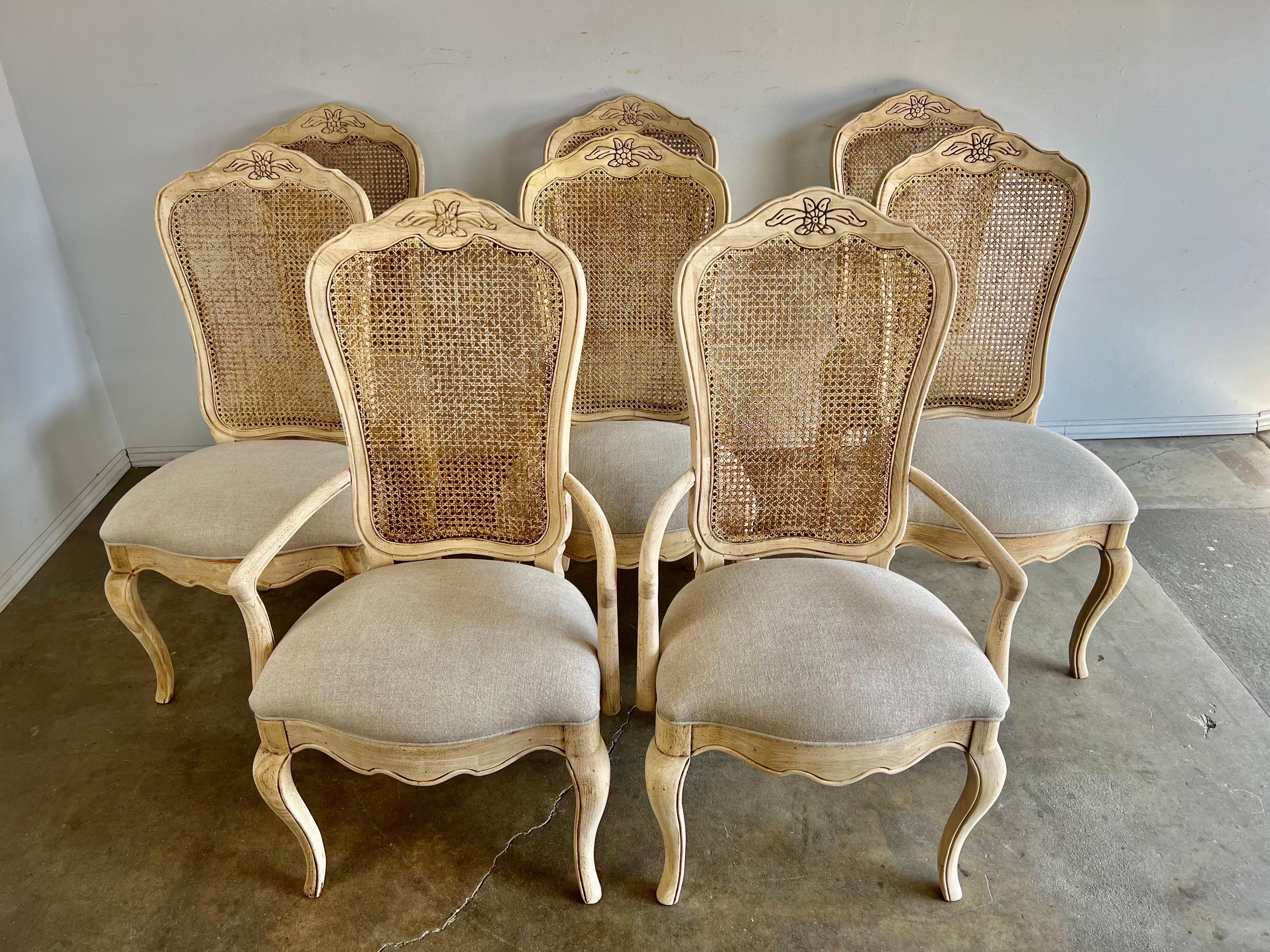 Set of eight French cane back dining chairs.  The chairs are newly upholstered in a washed Belgium linen.  The chairs stand on four cabriole legs with a scalloped apron across the front.  There are flowers carved into the top portion of the frame. 