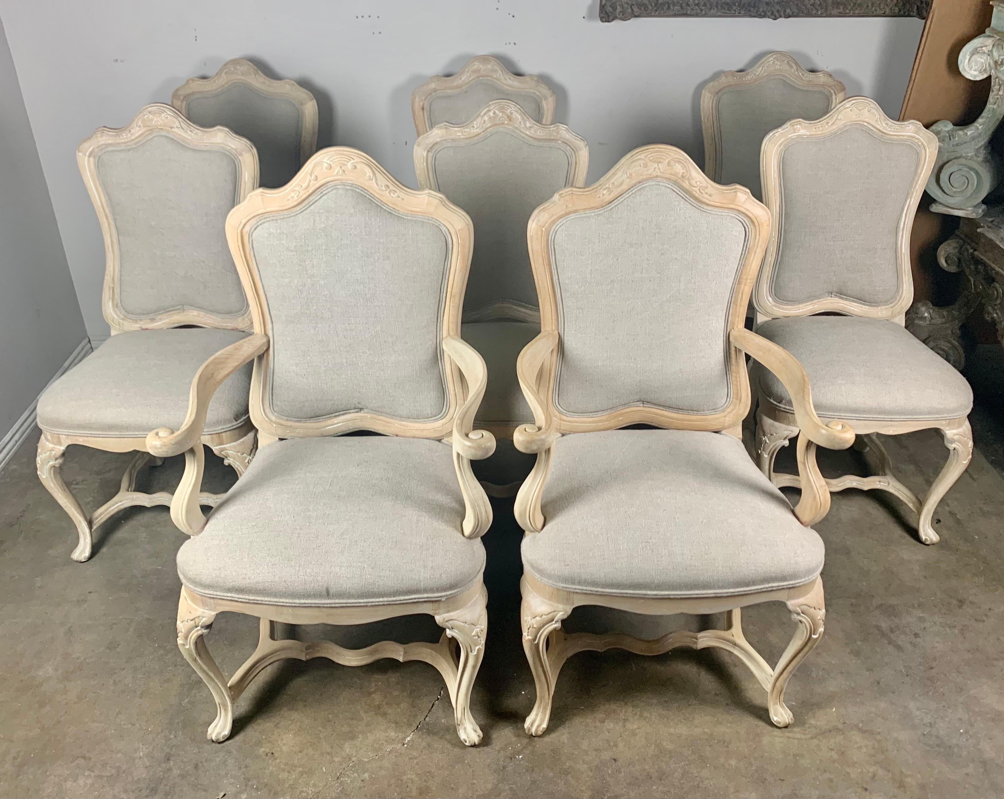 Set of eight bleached walnut French carved wood dining chairs. The chairs stand on cabriole legs and are connected by a bottom stretcher. The chairs are newly reupholstered in a washed Belgium linen with nailhead trim detail.

Size of armchairs: