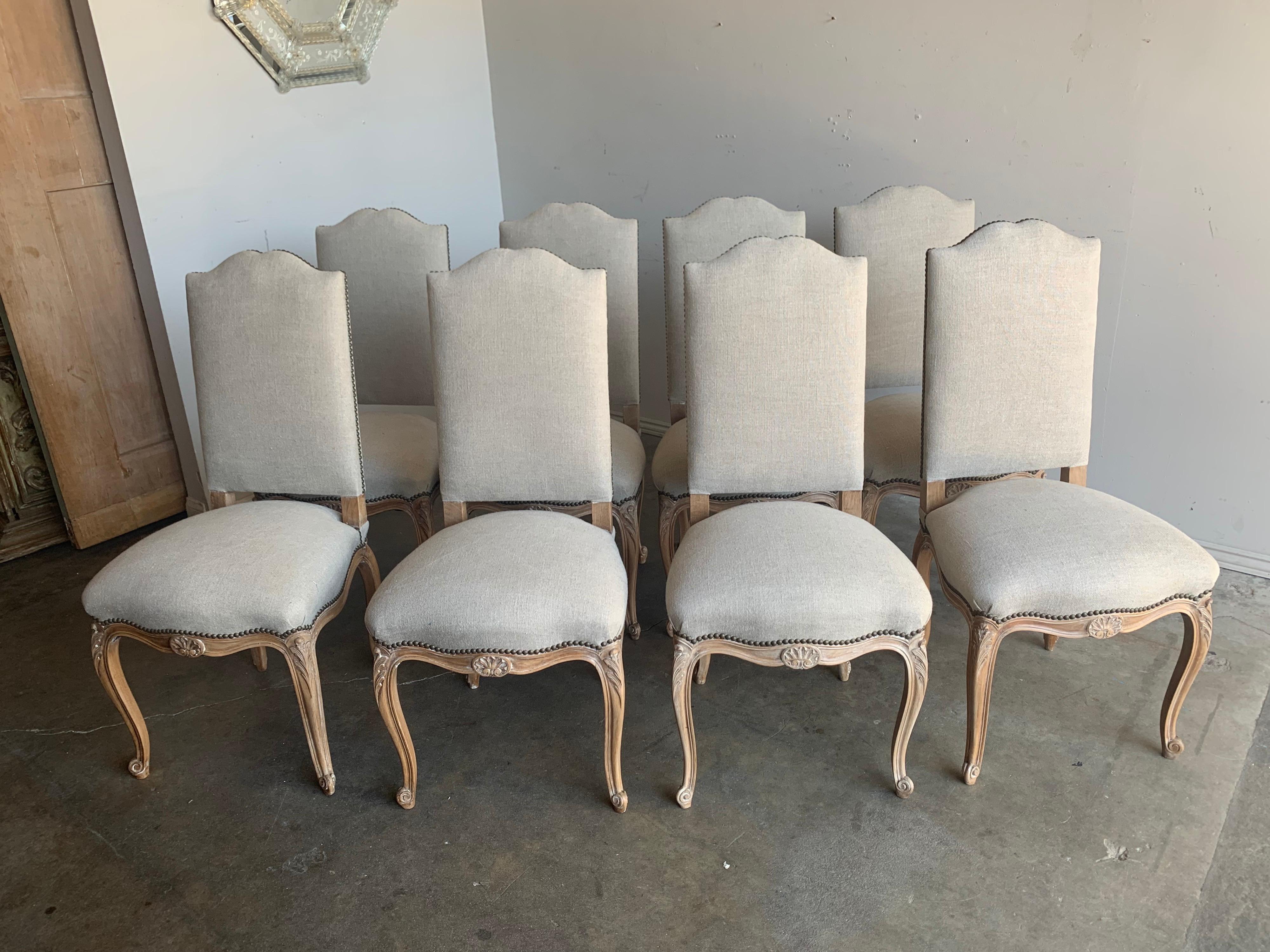 Set of eight French carved dining side chairs newly reupholstered in a washed Belgium linen. The chairs stand of four cabriole legs that end in rams feet.