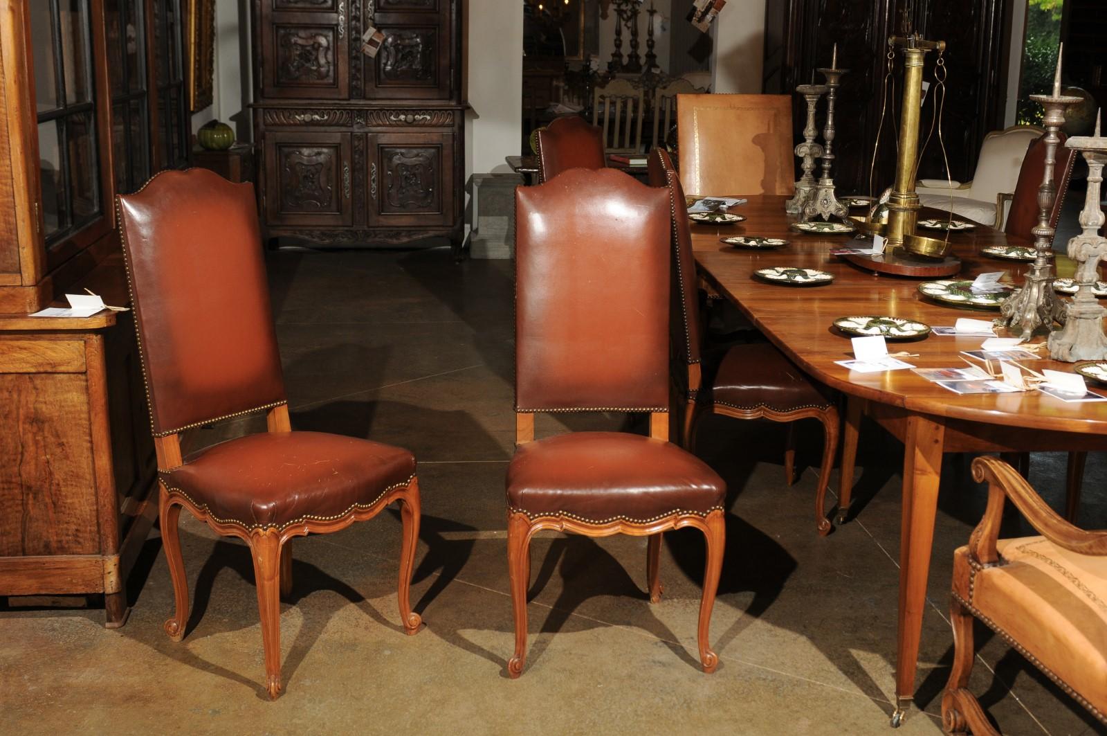 A set of eight French Louis XV style walnut dining room chairs from the 19th century, with leather upholstered seats and backs, and cabriole legs. Born during the 19th century, this set of French dining room side chairs presents the stylistic traits