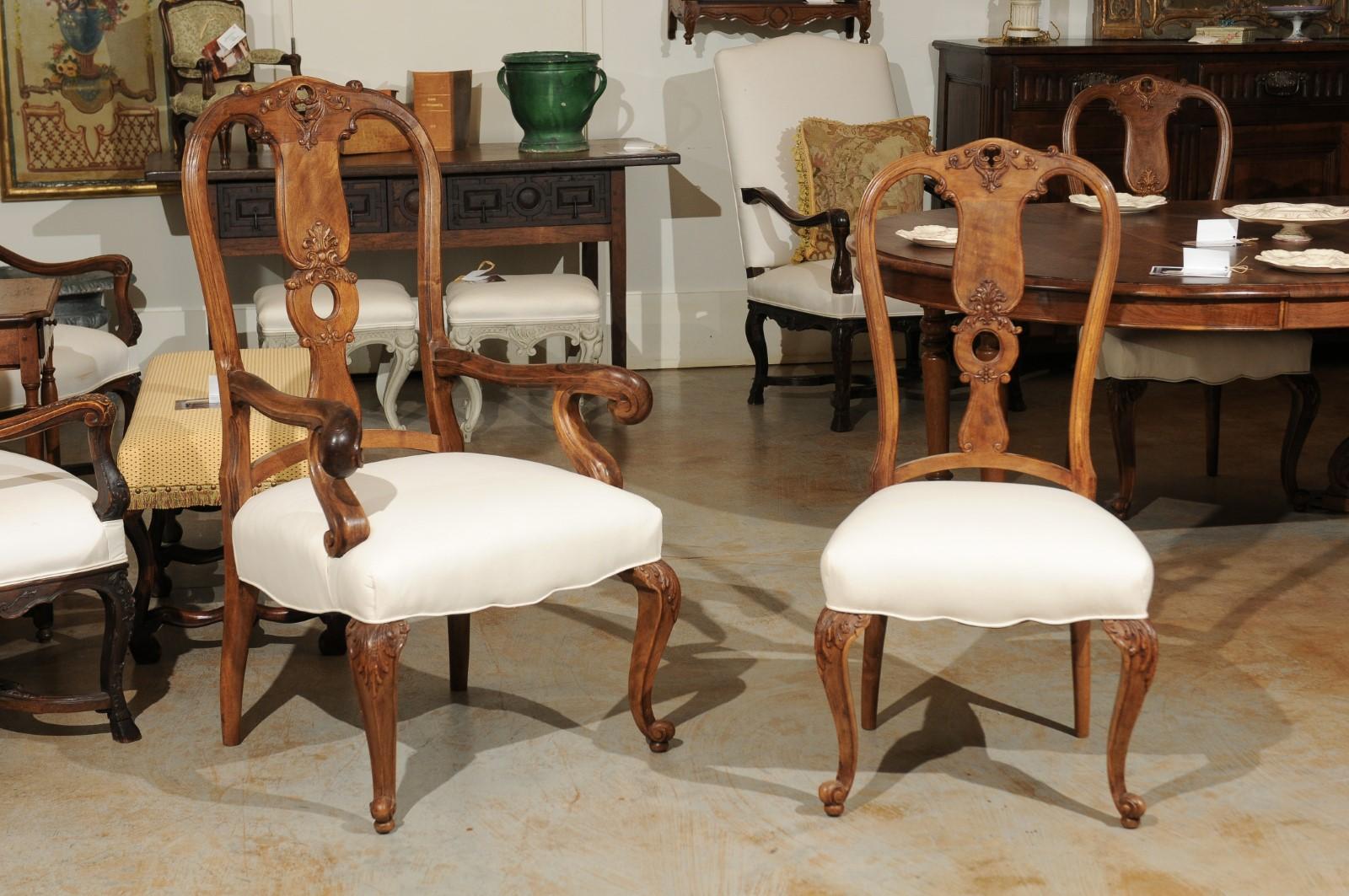 A set of eight French Rococo style walnut dining room chairs from the 19th century, with carved and pierced splats, cabriole legs and newly upholstered seats. This exquisite set of eight French dining chairs features six sides and two arms. Each