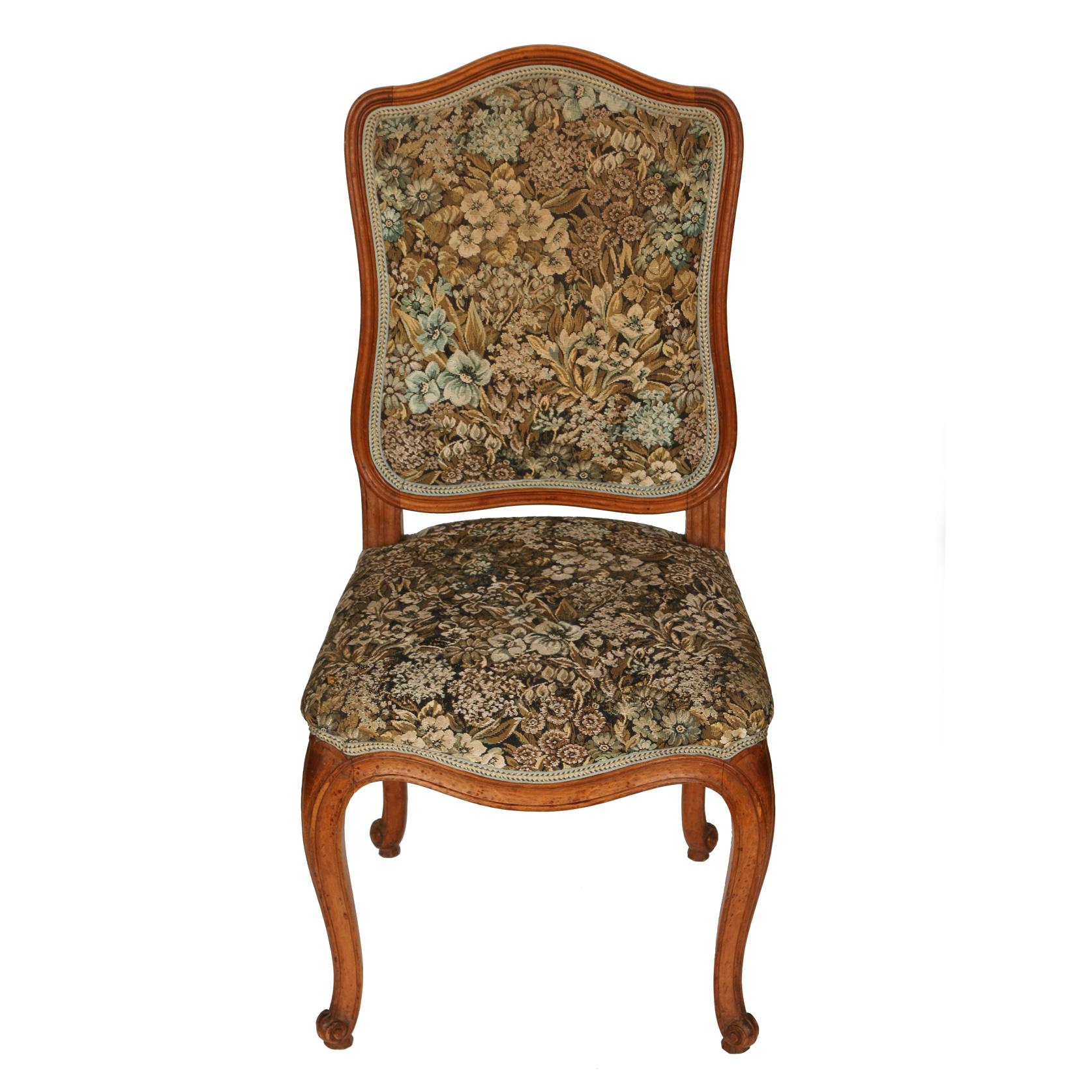A set of eight French upholstered dining chairs with curved back, seat apron and cabriole leg. Floral fabric in tones of gold, light brown and pale blue on a dark ground.