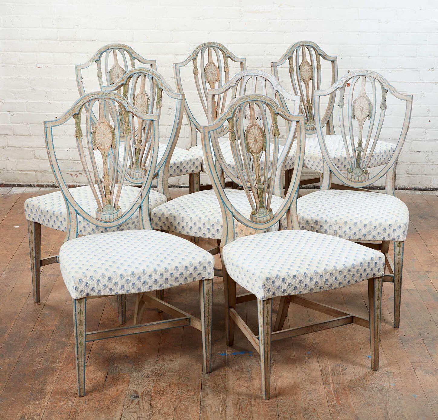 A rare set of eight Hepplewhite painted dining chairs. Pierced shield backs with early hand-painted leaf and vine decoration with central patera and blue border on white ground throughout. Shaped over-upholstered seats over square tapered legs with