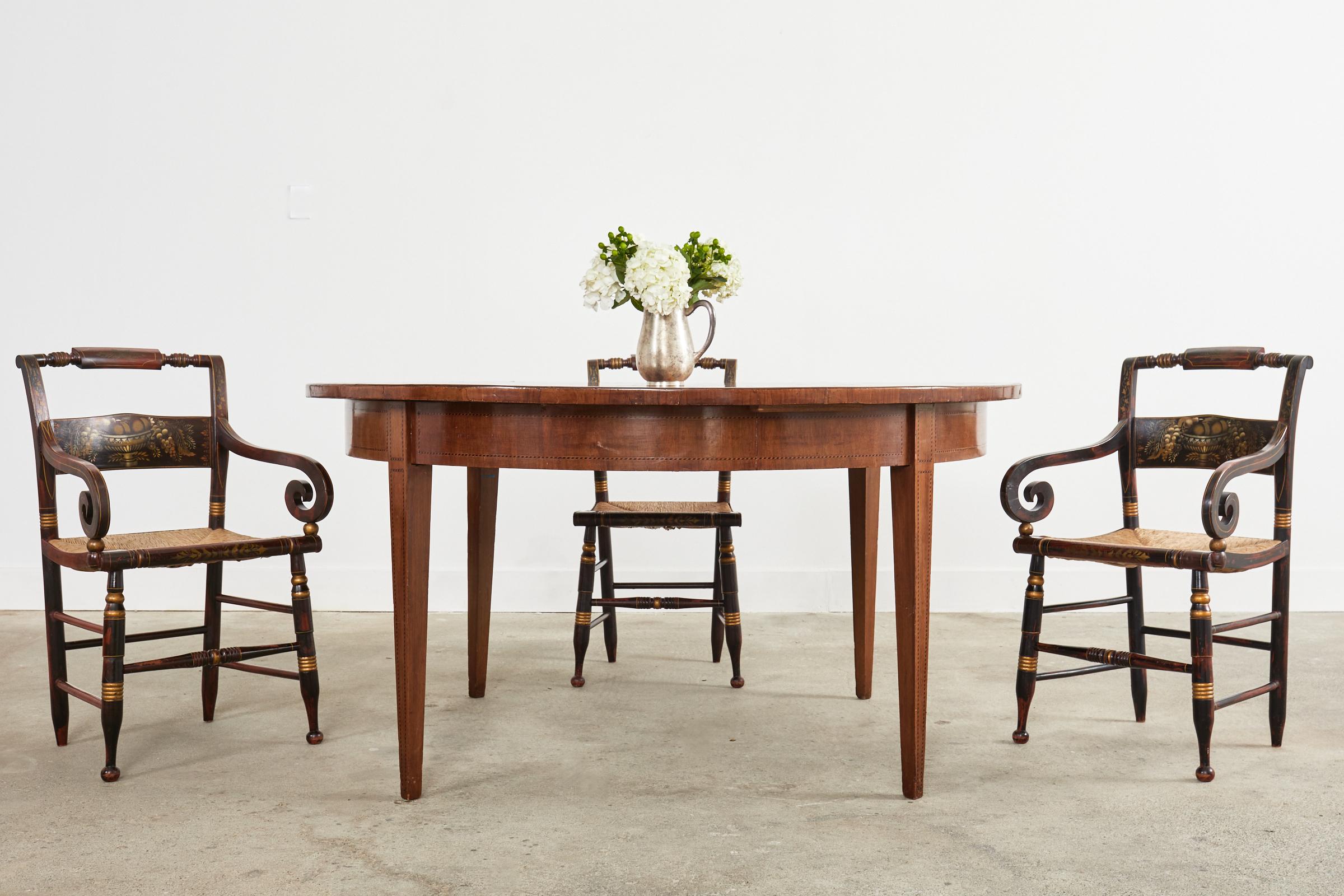 American classical set of eight New England style stenciled dining chairs made in the manner of Lambert Hitchcock. The painted chairs feature a rush seat and the frames are embellished with parcel gilt thread accents. The set consists of six side
