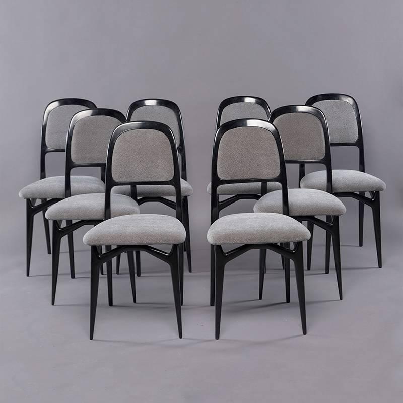 Set of eight circa 1950s Italian dining chairs with black lacquer frames that feature tapered legs, arched and padded seat backs and criss cross support rails beneath the seats. Chairs are newly upholstered in a pale gray nubby textured chenille.