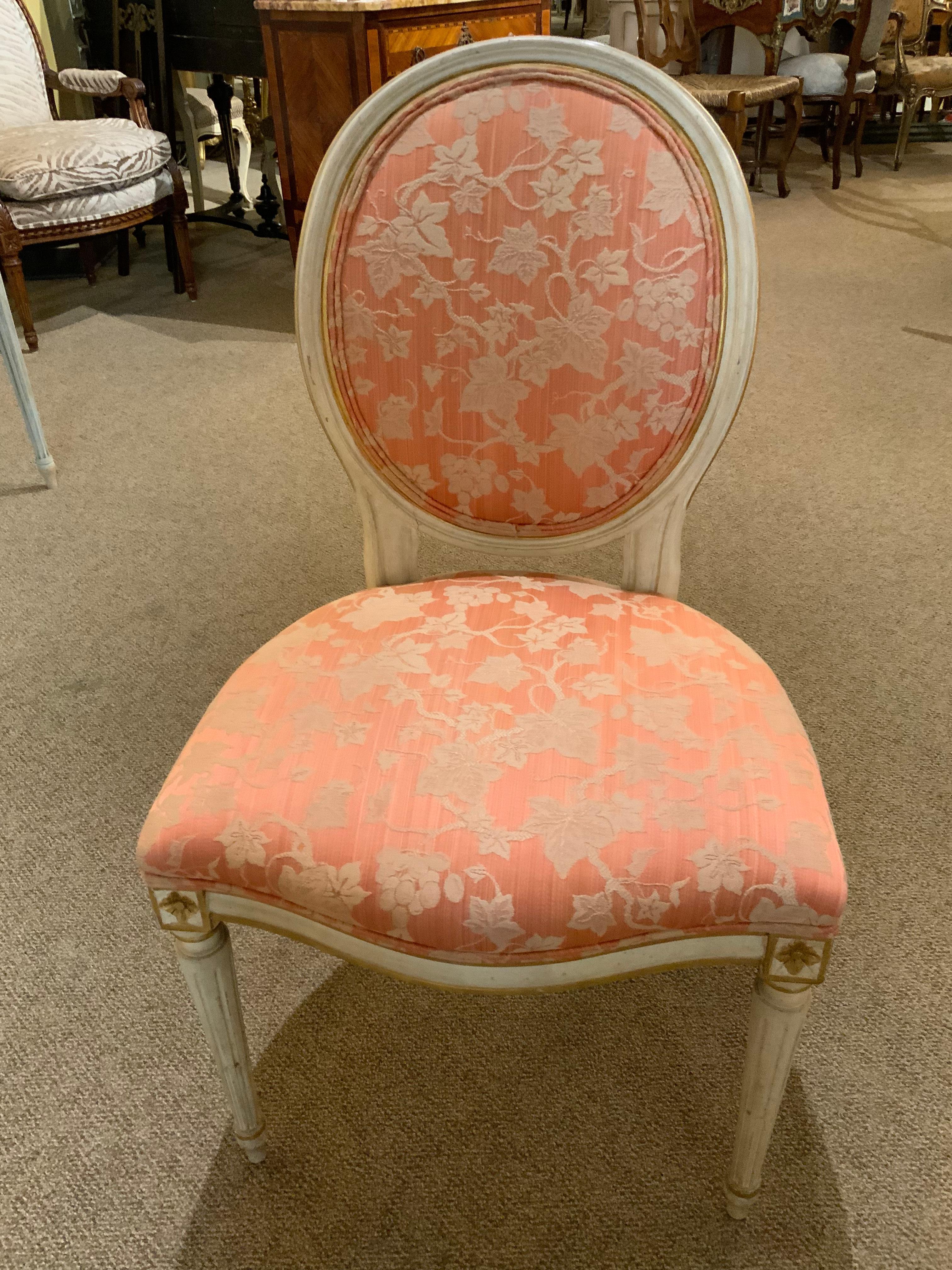 Set of eight upholstered dining chairs which include two high back
Host and hostess chairs. The six side chairs have an oval back
And they are painted in a cream/white hue, With gilt trim at the
Four corners of each leg. The host chairs are in a