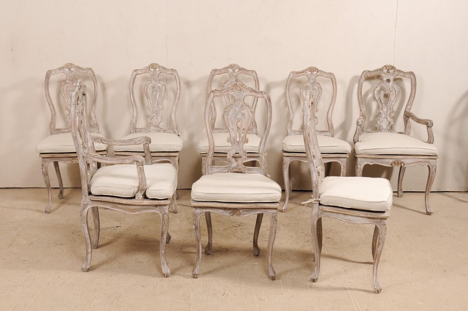 A set of eight Italian midcentury carved dining chairs with cane seats, and custom seat cushions. This set of eight chairs from Italy is comprised of a pair of arm chairs along with six side chairs. Each chair features a shapely wood back and top