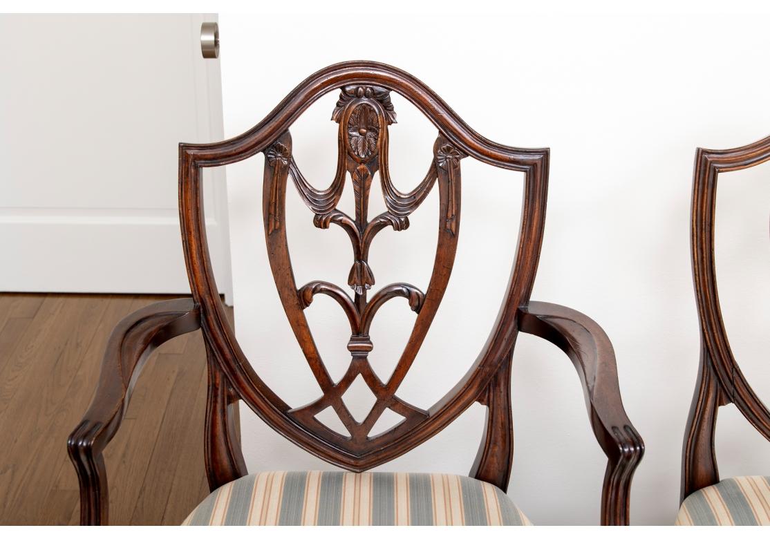 A exceptionally graceful and stately set from Bevan Funnell. Set of eight mahogany shield back dining chairs from Bevan Funnell featuring six side chairs and two arm chairs with shield back carved with floral medallion and swag motif on tapered
