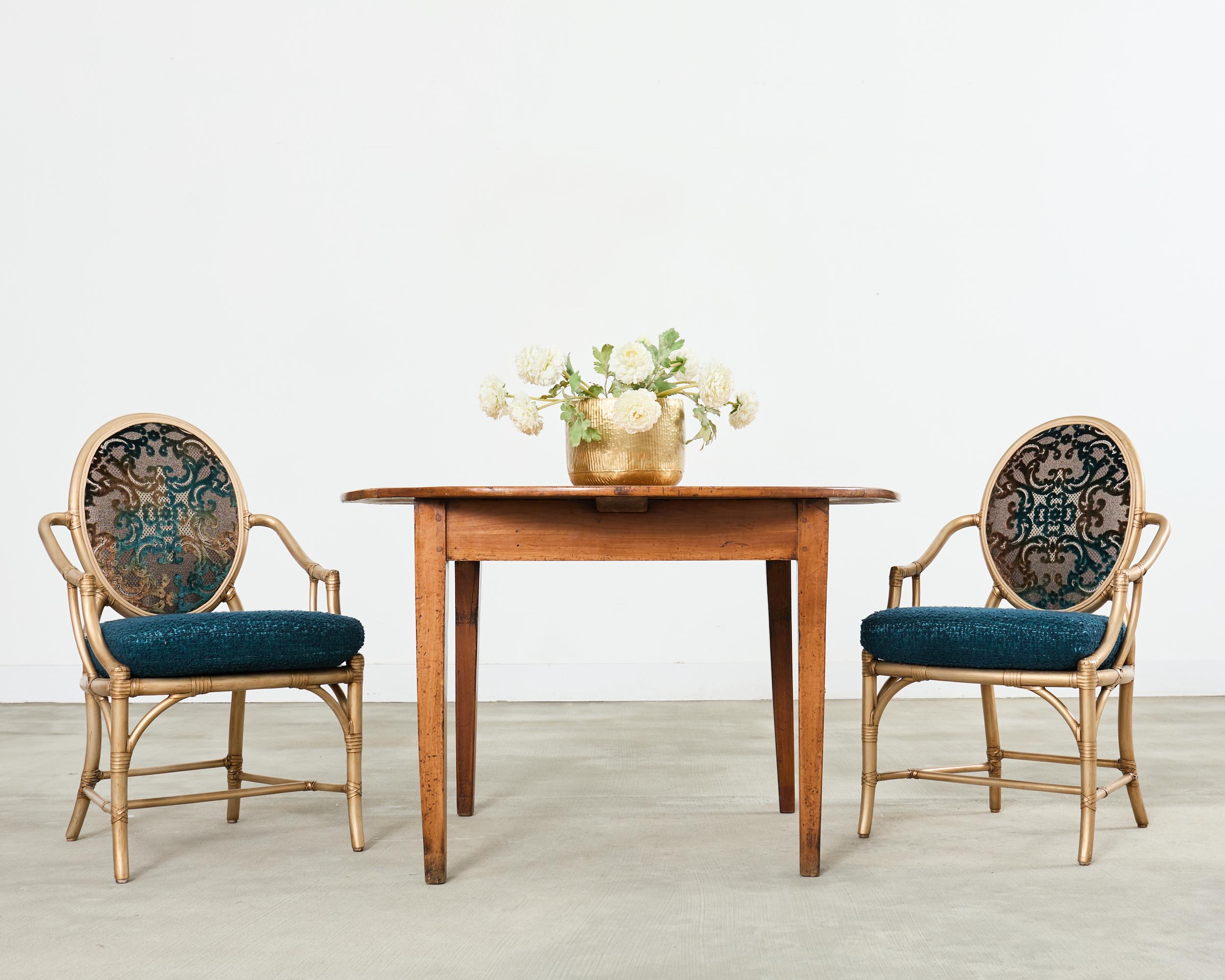 Dramatic and opulent set of eight McGuire rattan and cane dining chairs featuring a gilt lacquer finish. The chairs have a round cameo or balloon back with a caned back and seat. The seat is fitted with a deep, loose seat cushion upholstered with a
