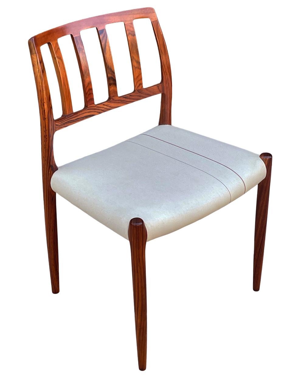 A complete set of 8 dining chairs designed by Neils O. Möller and produced in Denmark circa 1960's. These feature solid rosewood construction with original fabric seat cushions. The sculpted backs are the absolute highlight of these chairs. Fabric