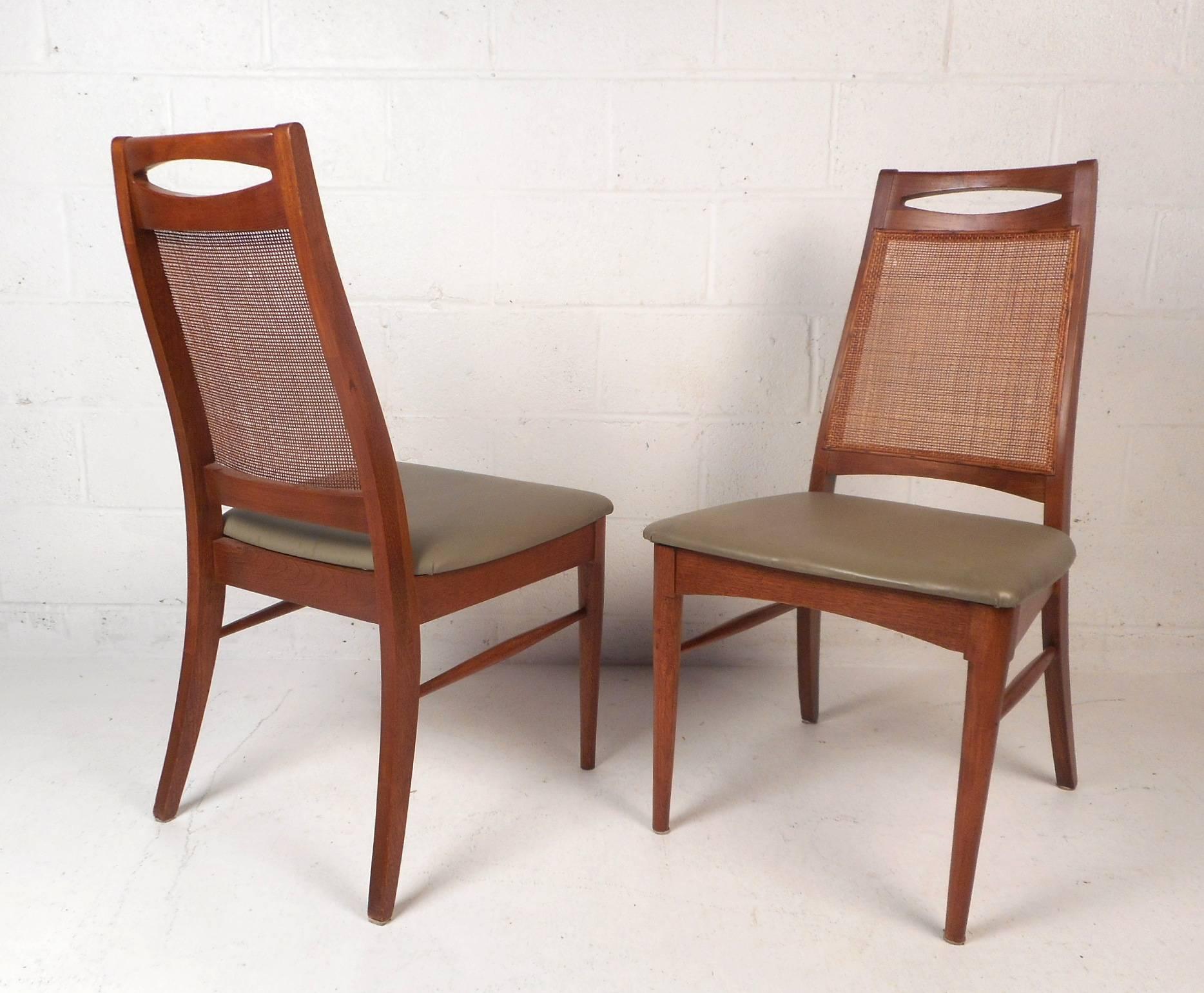 This gorgeous midcentury set includes six dining chairs and two armchairs. A very unique design with an oblong cut-out by the head rest and a cane backrest. The sculpted walnut frame has tapered stretchers connecting the front legs to the back legs.