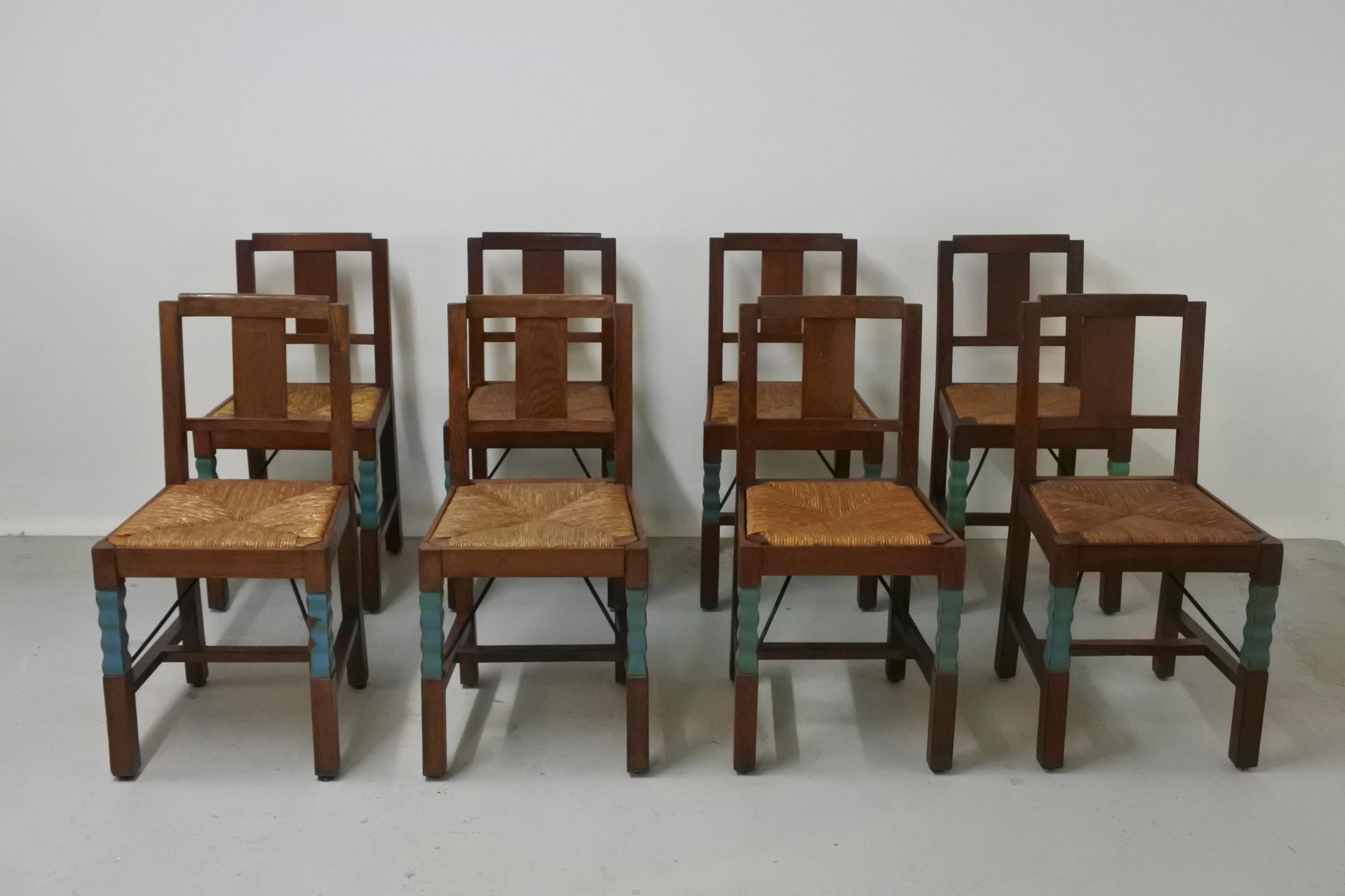 Set of eight dining chairs in the style of French woodworker Joseph Savina.

Oak wood and rush seats. Carved and painted front legs.
Beautiful details.

A metallic structure was added under the seat in the 1950s to preserve the chairs. 
They