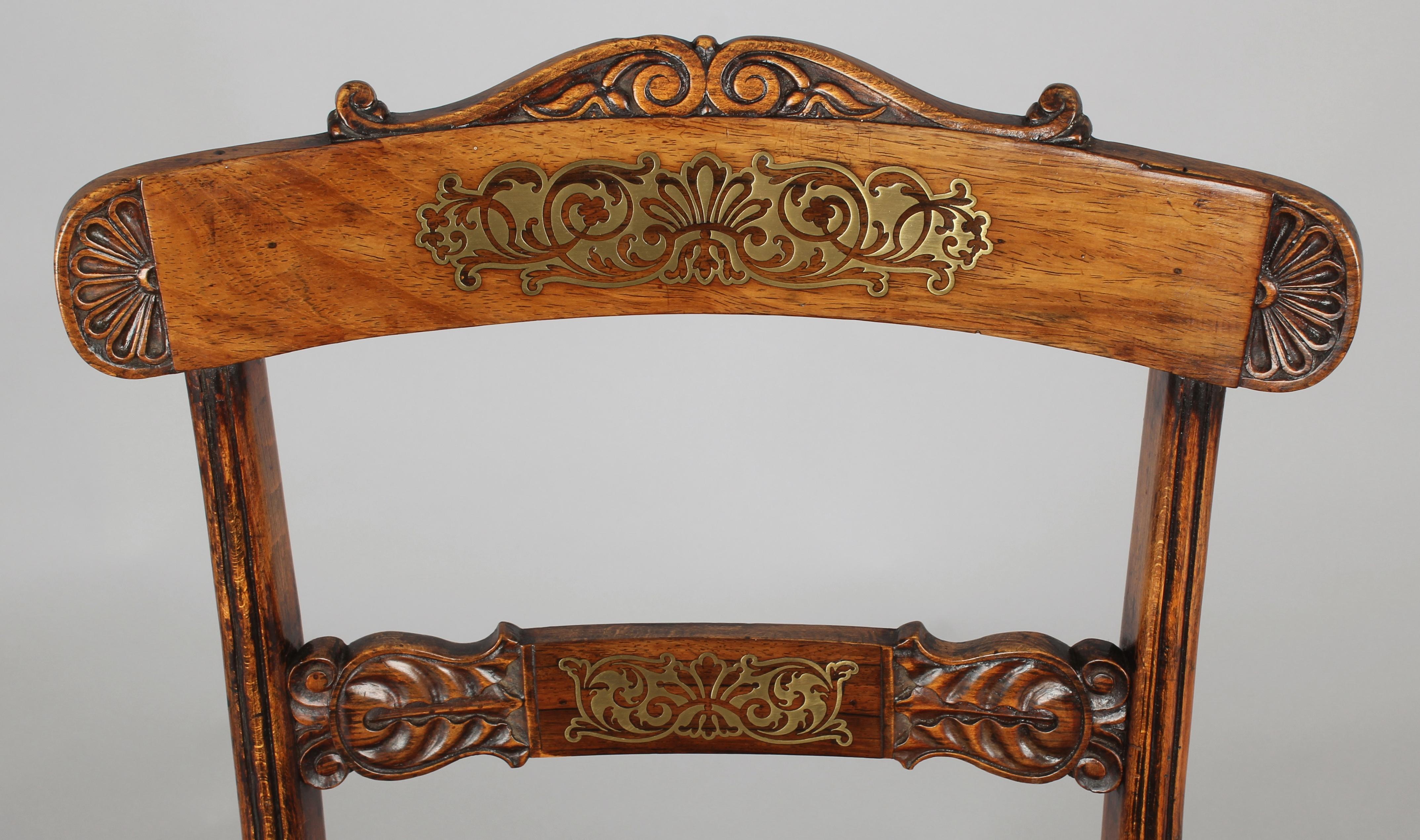 Set of eight Regency period simulated rosewood and brass inlaid chairs; the backs with carved lunette, foliate and scrolled decoration, and the overhanging top-rails and mid-rails with inlaid cut-brass arabesque panels on grounds of rosewood veneer.