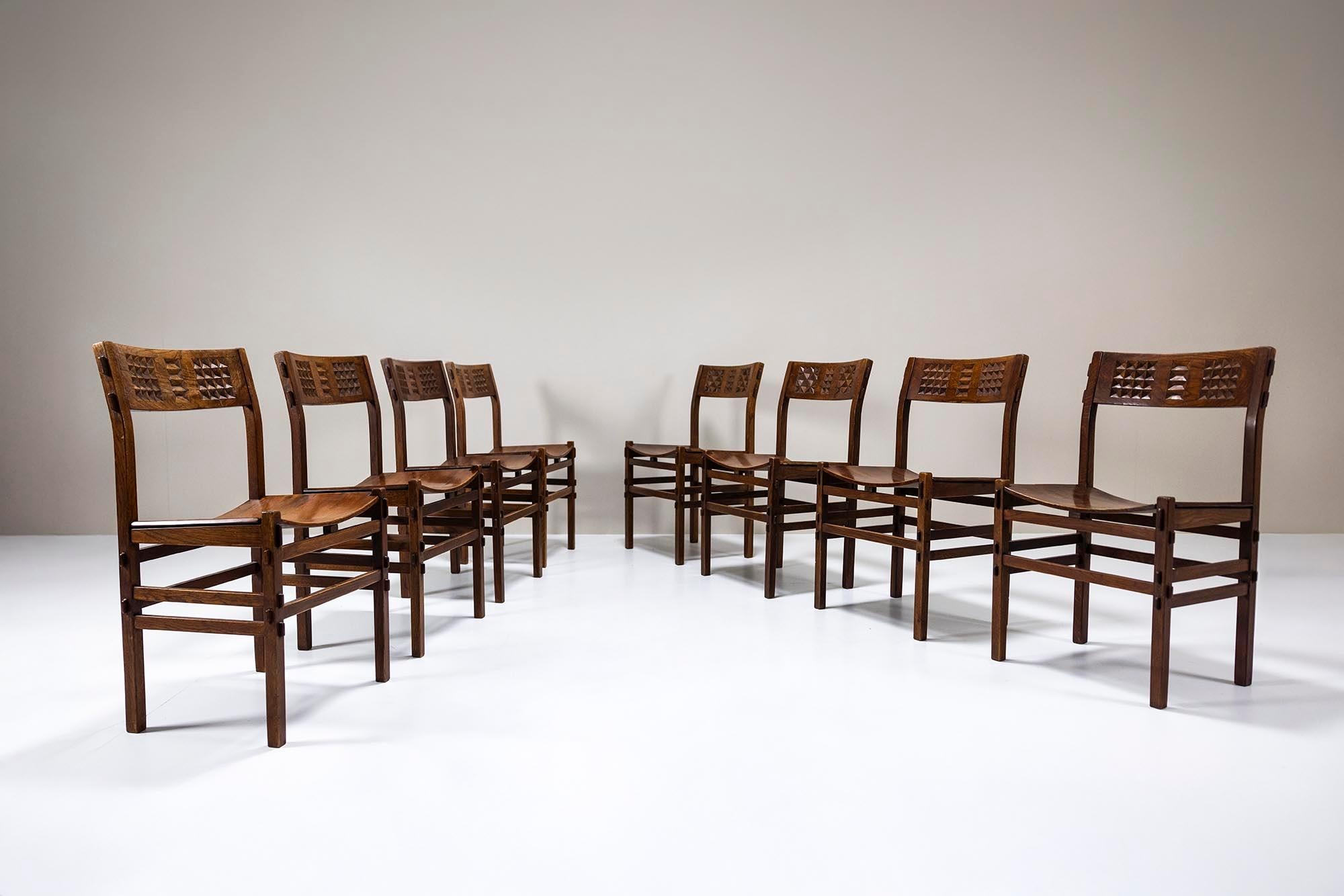 Un set di otto sedie Rivadossi, realizzate in rovere di Slavonia negli anni '70, che mostrano una patina impressionante che parla della loro storia. Questi pezzi incarnano un equilibrio unico tra solida artigianalità e forma scultorea, una firma