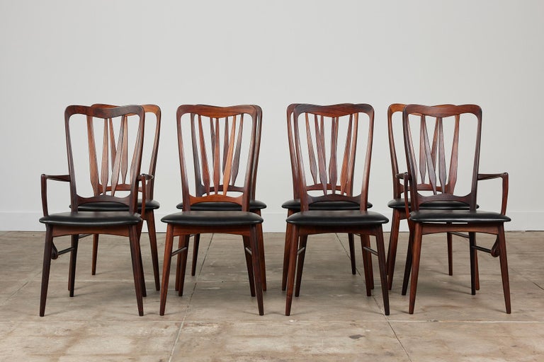 Set of eight Niels Koefoed “Ingrid” dining chairs in rosewood, c.1960s, Denmark for Koefoeds Hornslet. The set consists of six side chairs and two armchairs. All chairs feature sculpted rosewood frames with black Naugahyde on the seats. The