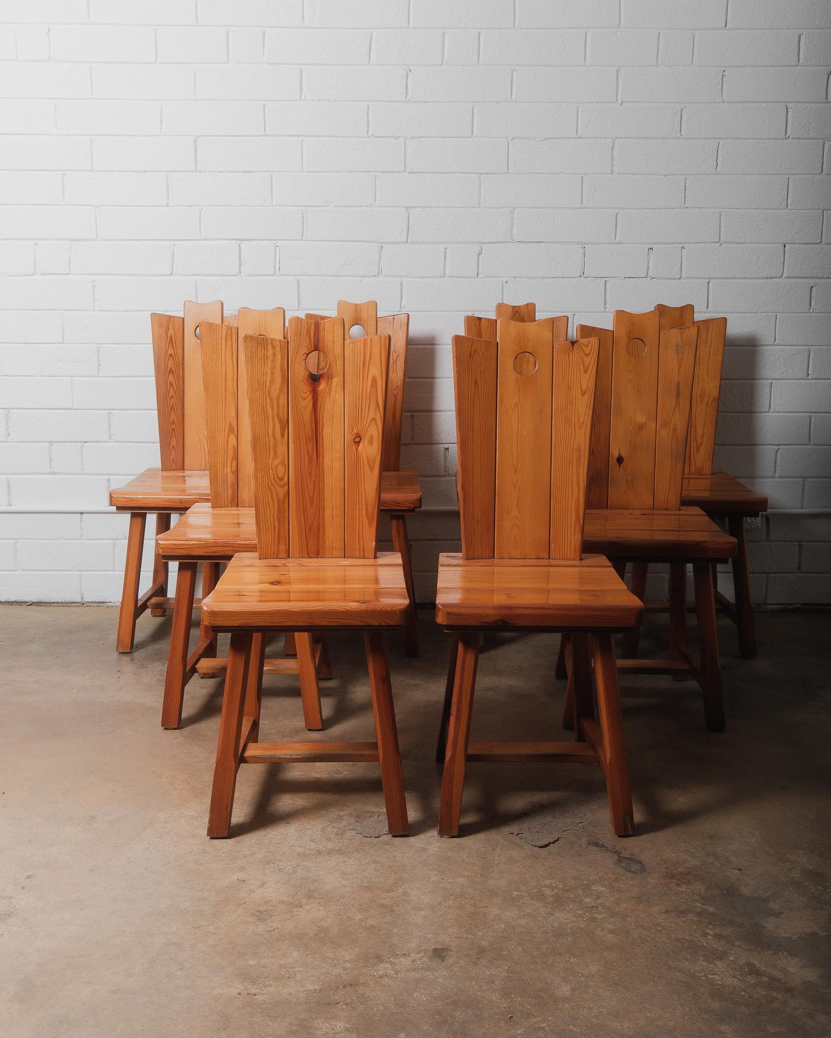 This set of eight handcrafted pine dining chairs showcases a charming rustic Alpine style, reminiscent of traditional Swiss and Austrian chalet furniture. Each chair features a high, slightly tapered backrest with a signature circular cutout at the
