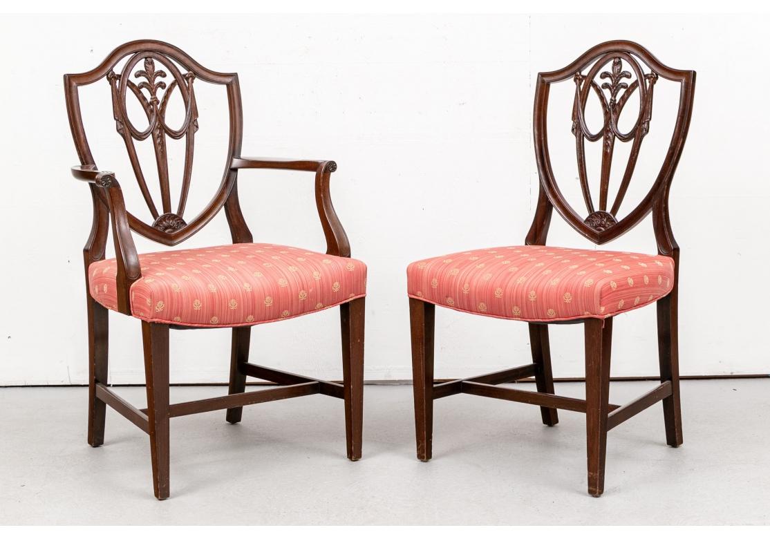 A particularly fine set of well made Sheraton style Shield Back Dining Chairs. Two arm and six side chairs. The shield backs with interlaced open swags and center tiered feather motifs over bell flowers. Demilune acanthus leaf decorated ends. Raised