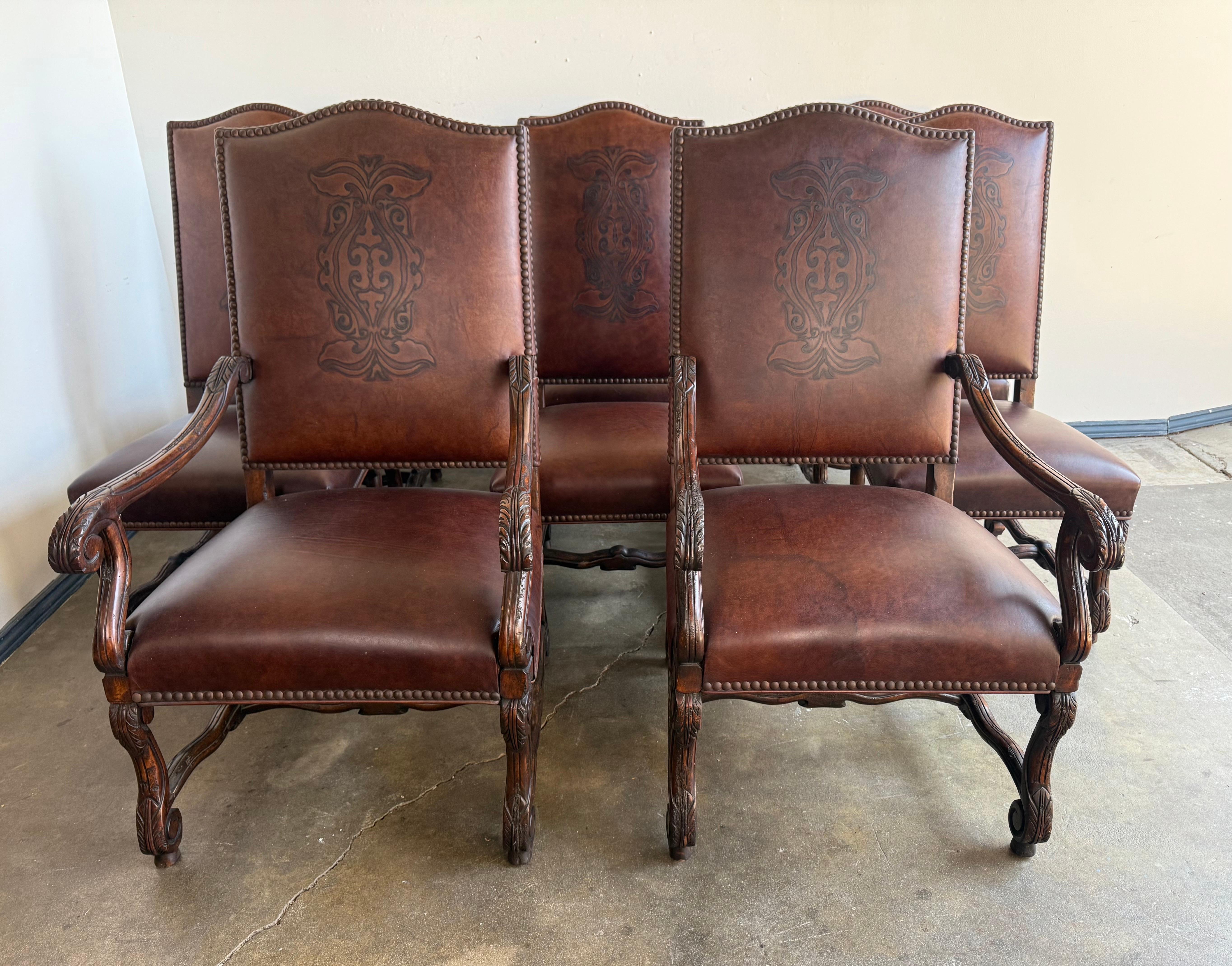A handsome set of eight Spanish Revival dining chairs, comprised of two armchairs and six side chairs, crafted in the early 20th century. Executed in richly patinated walnut, each chair features beautifully carved frames with scrolling arms, foliate
