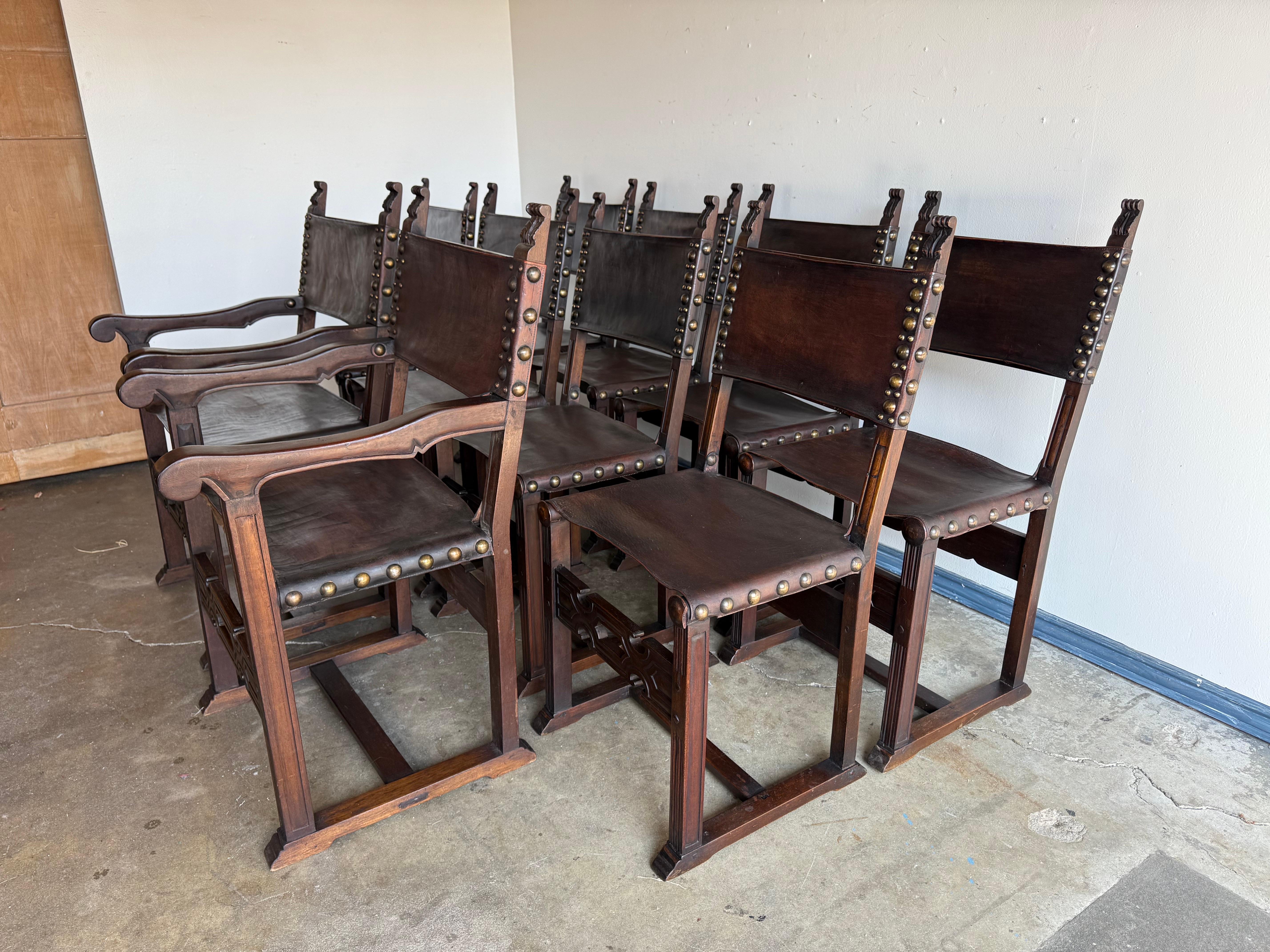 Un consistente set di otto sedie da pranzo in stile Revival spagnolo, composto da sei sedie laterali e due poltrone. Ogni sedia è caratterizzata da una solida struttura in legno duro tinto di scuro con stiracoli geometrici intagliati, gambe