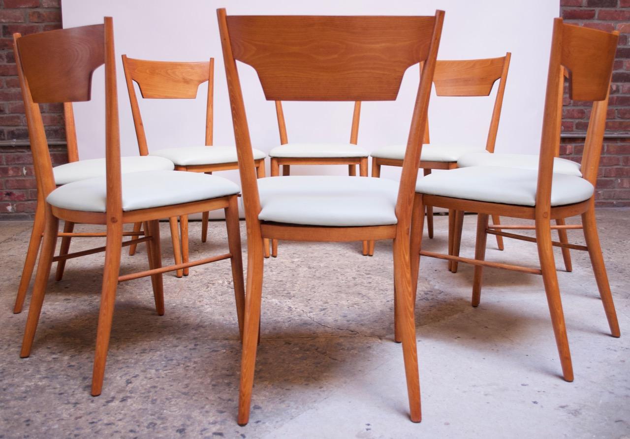 Set of eight stained maple dining chairs designed by Paul McCobb for his Perimeter Group and manufactured by Winchendon Furniture (circa 1957). Shapely backrests and long tapered legs add dramatic lines to an otherwise modest design. Maple has been
