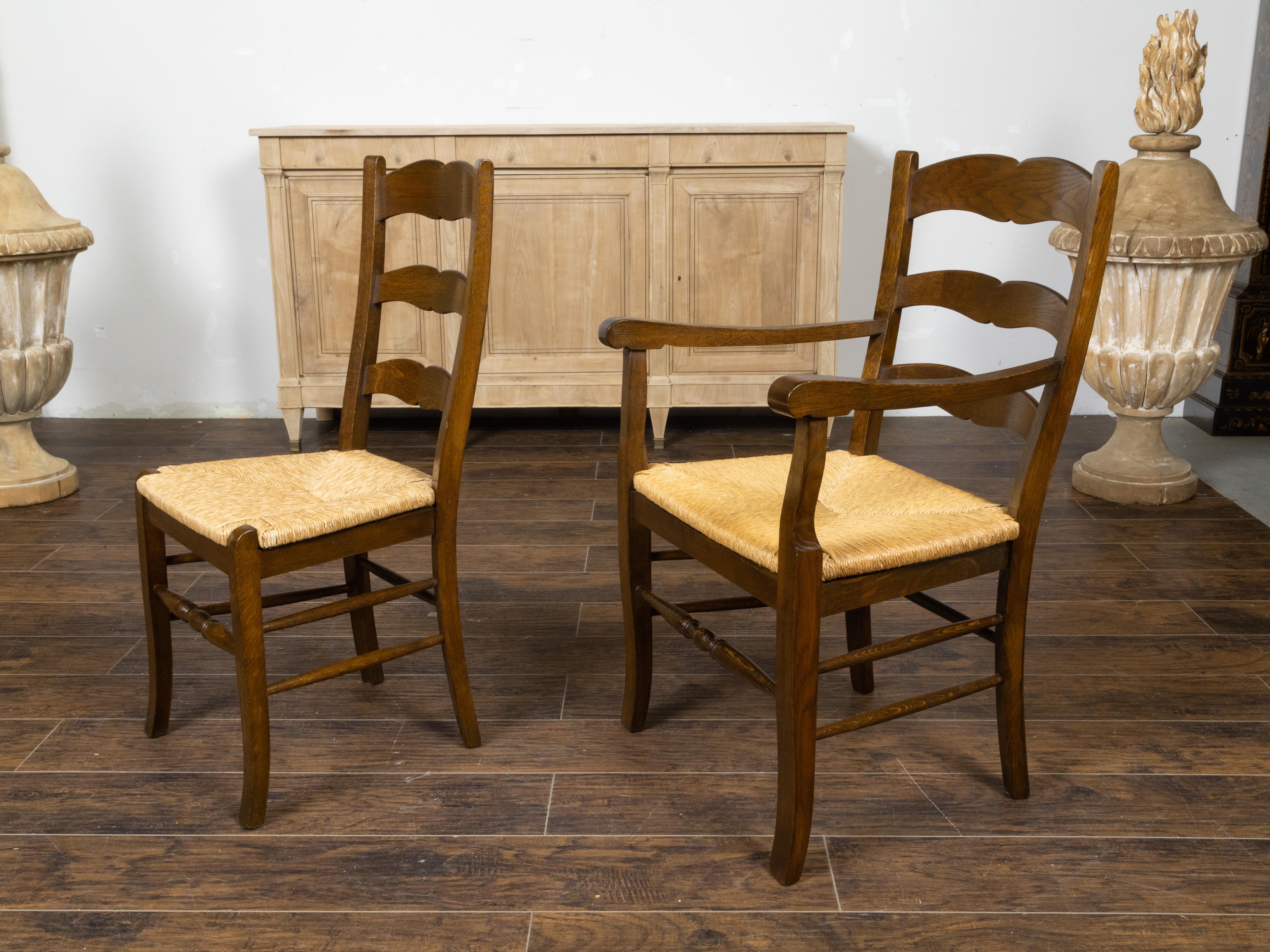 A set of eight English oak ladder back dining room chairs from the early 20th century, with rush seats and comprising of two armchairs and six sides. Created in England during the Turn of the Century which saw the transition between the 19th to the