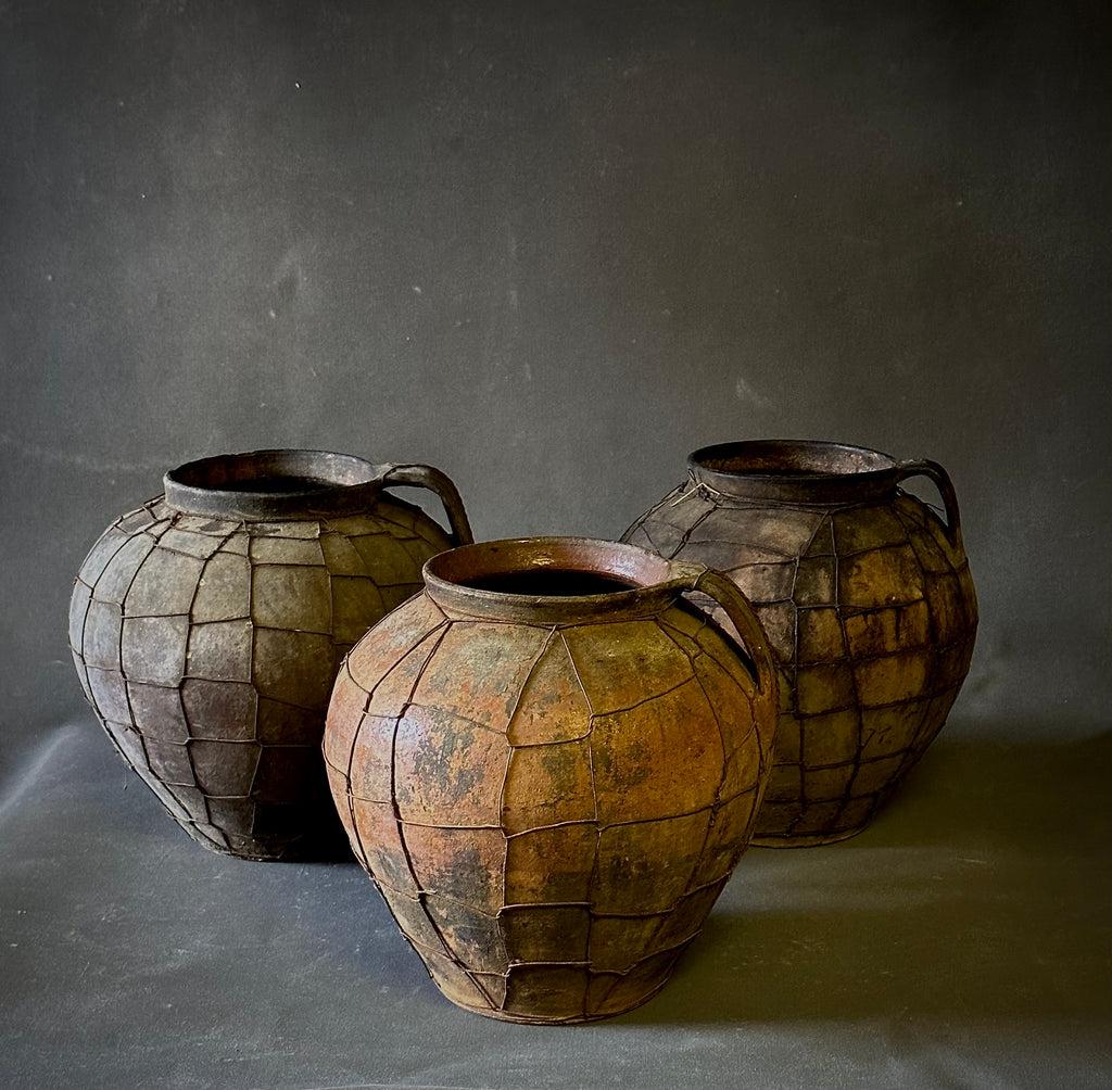 Queste pentole di terracotta ucraine dell'inizio del XX secolo, avvolte in una rete metallica utilitaria, evocano un forte senso di tradizione e artigianalità. Originariamente progettati per un uso pratico, la loro struttura robusta e la loro patina