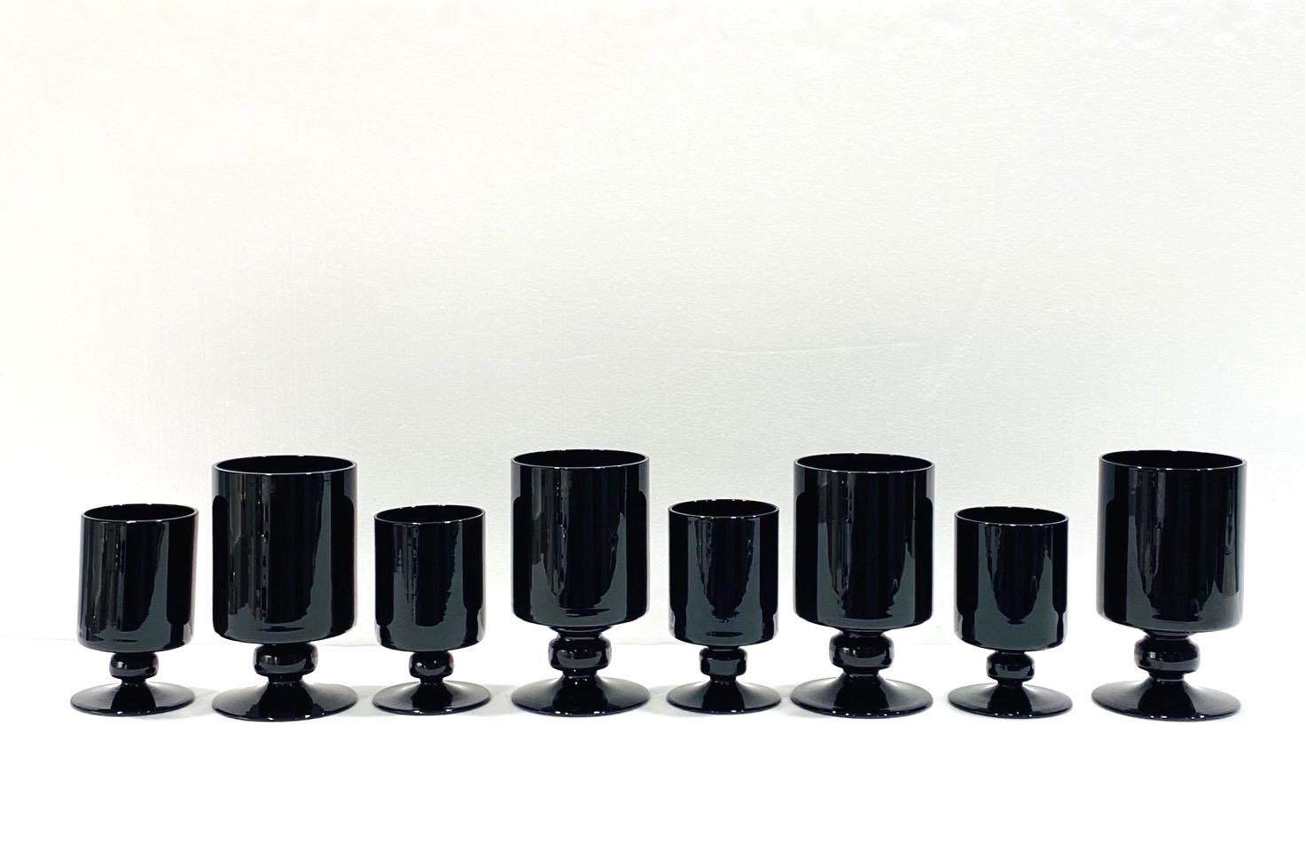 Set of eight vintage blown stemware glasses in black opaque crystal. Hollywood Regency style barware set includes four wine glasses and four larger water goblets. The glasses feature cylinder bowls with short stylized stems and solid weight. Makes a