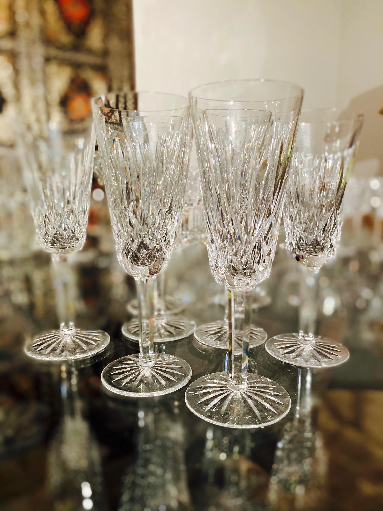 Set of eight luxury crystal champagne flutes from Waterford Crystal, circa 1995. The Lismore Collection is perhaps Waterford's most distinguished design featuring hand blown crystal with the pattern's signature diamond and wedge cuts. First