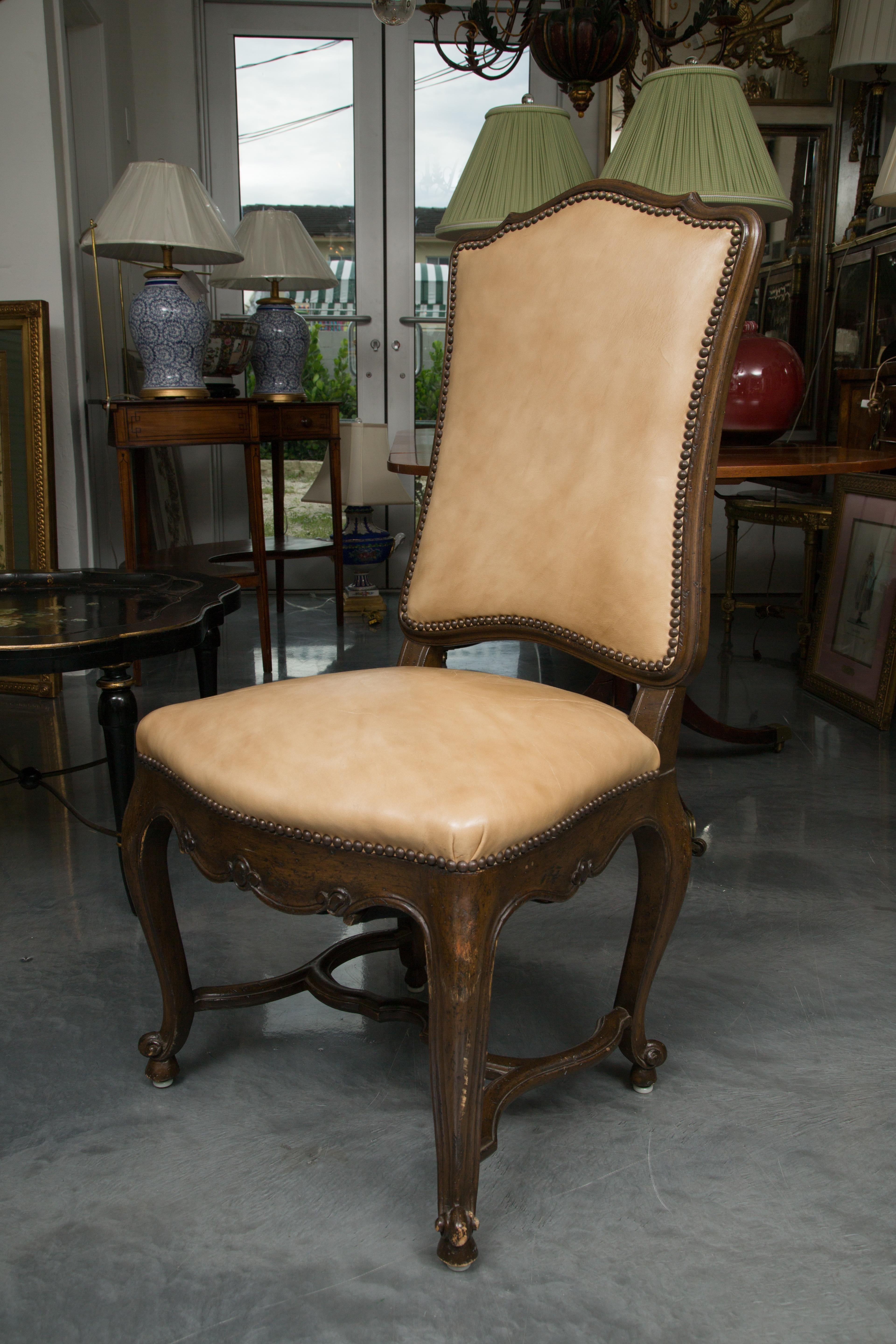 This is a sophisticated, yet mellow, set of eight walnut French Louis XV dining side chairs, the shaped top rail over a leather-upholstered back secured with brass nail heads, above a fully padded leather seat secured with brass nail heads over a