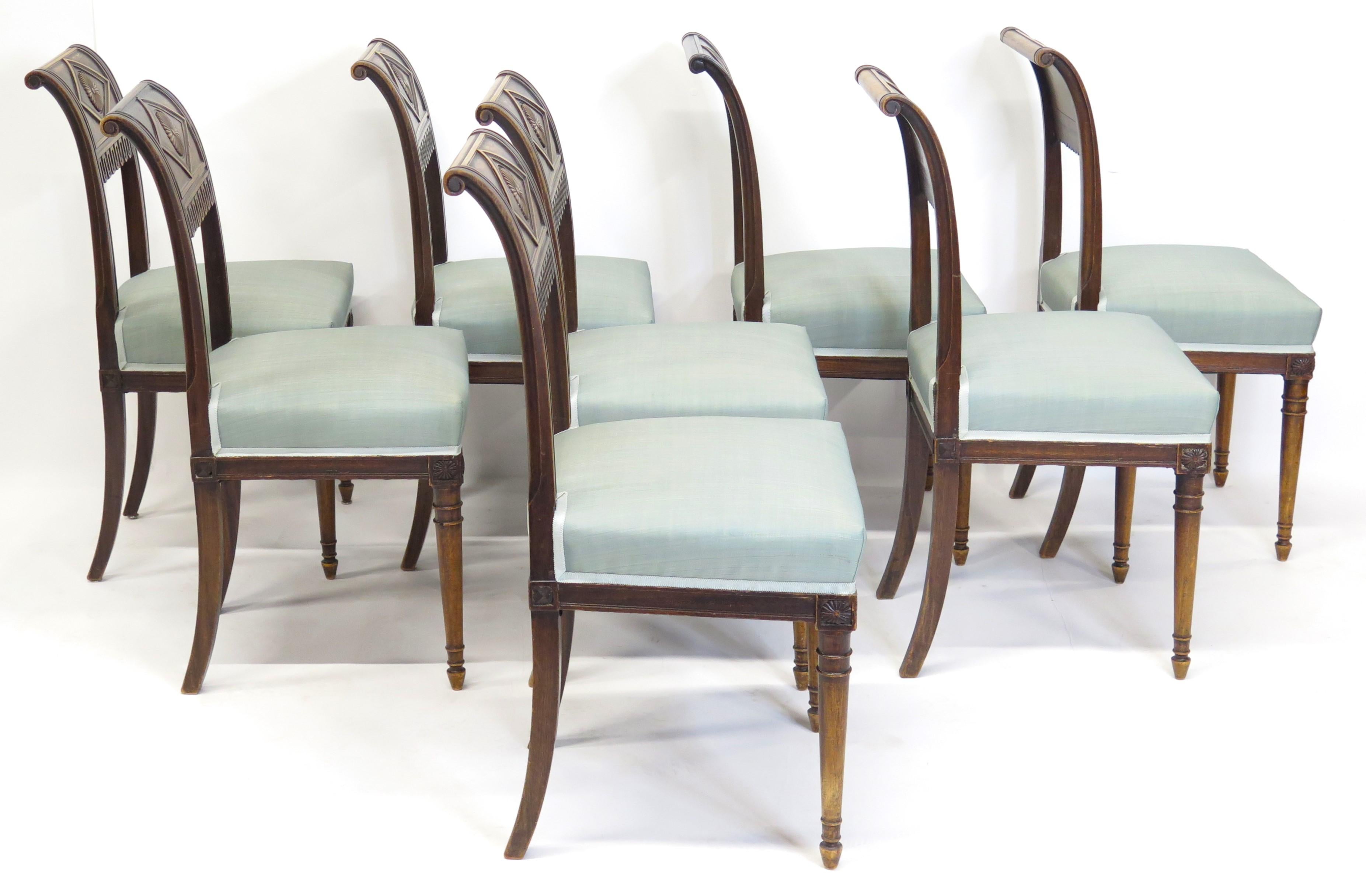 Set of eight walnut Neoclassical chairs the slightly bent backrests are decorated with hand-carved decor showing a rosette in a diamond shaped field and a lambrequin motif. This design and motif was developed by the French furniture maker Henri