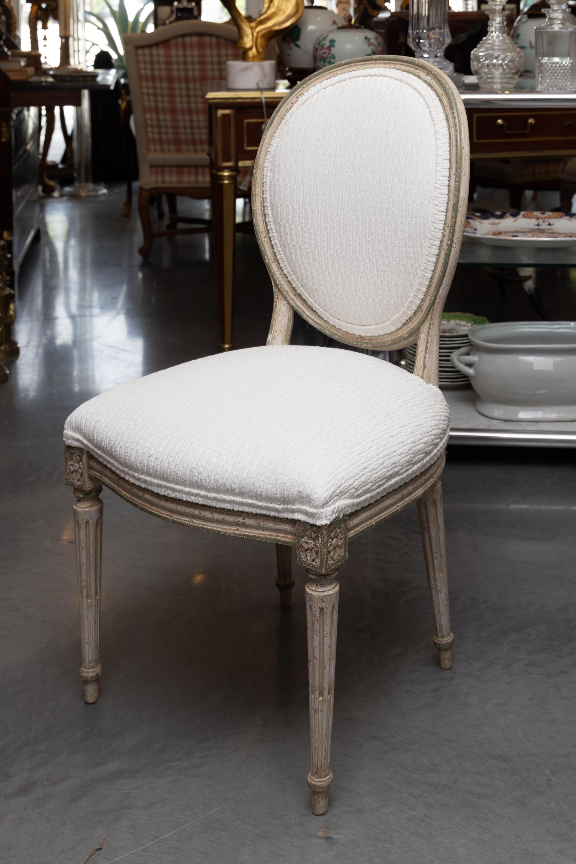 This is a lovely set of eight vintage, upholstered French white-painted Louis XVI style dining chairs with round, straight fluted legs and upholstered seat and padded back.  The set of chairs is comprised jof two arm chairs and six side chairs. 