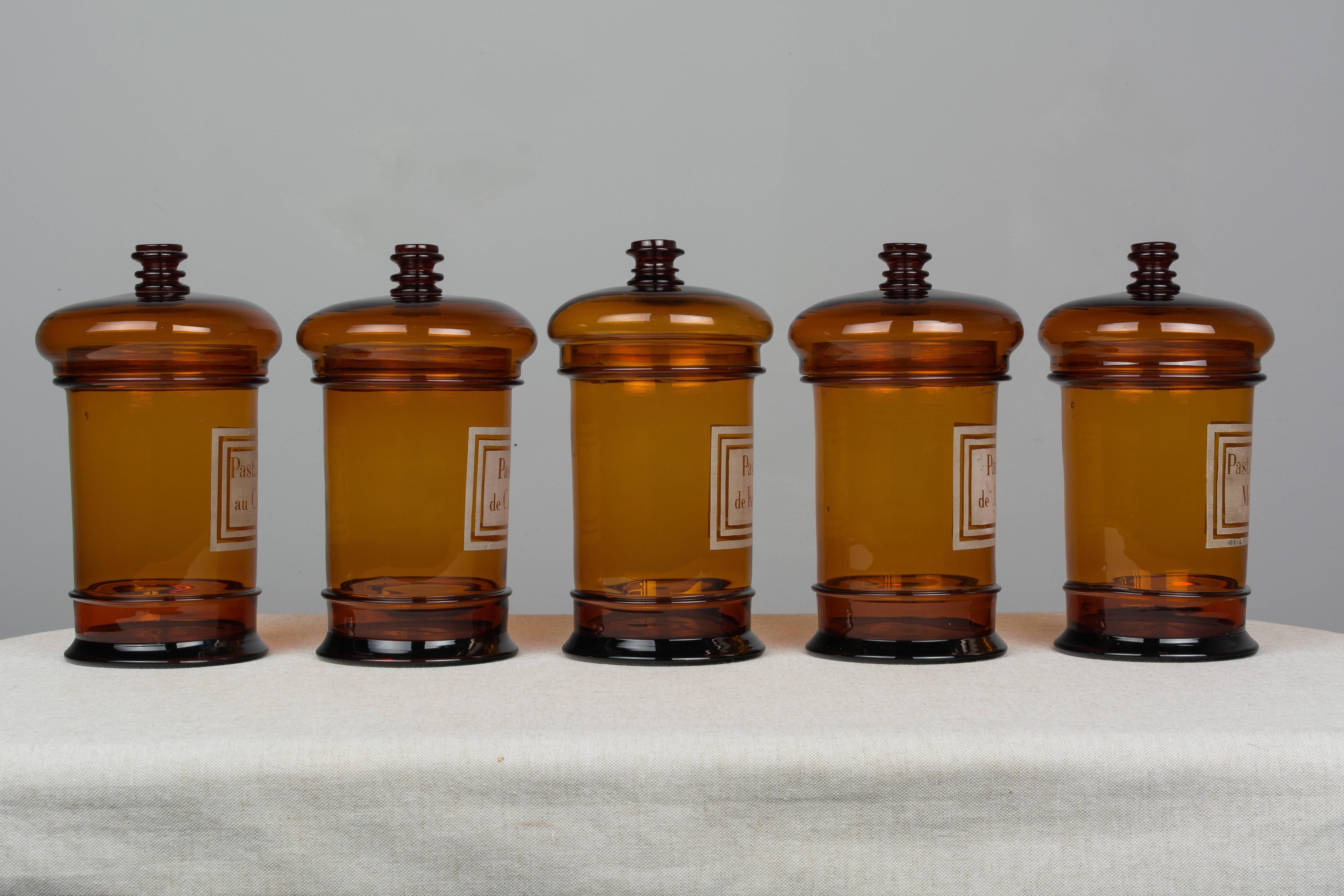 A set of five 19th century French amber glass apothecary jars with white stenciled labels and their lids. In excellent condition. Please refer to photos for more details. We have a large selection of French antiques at Olivier Fleury, Inc.  Please