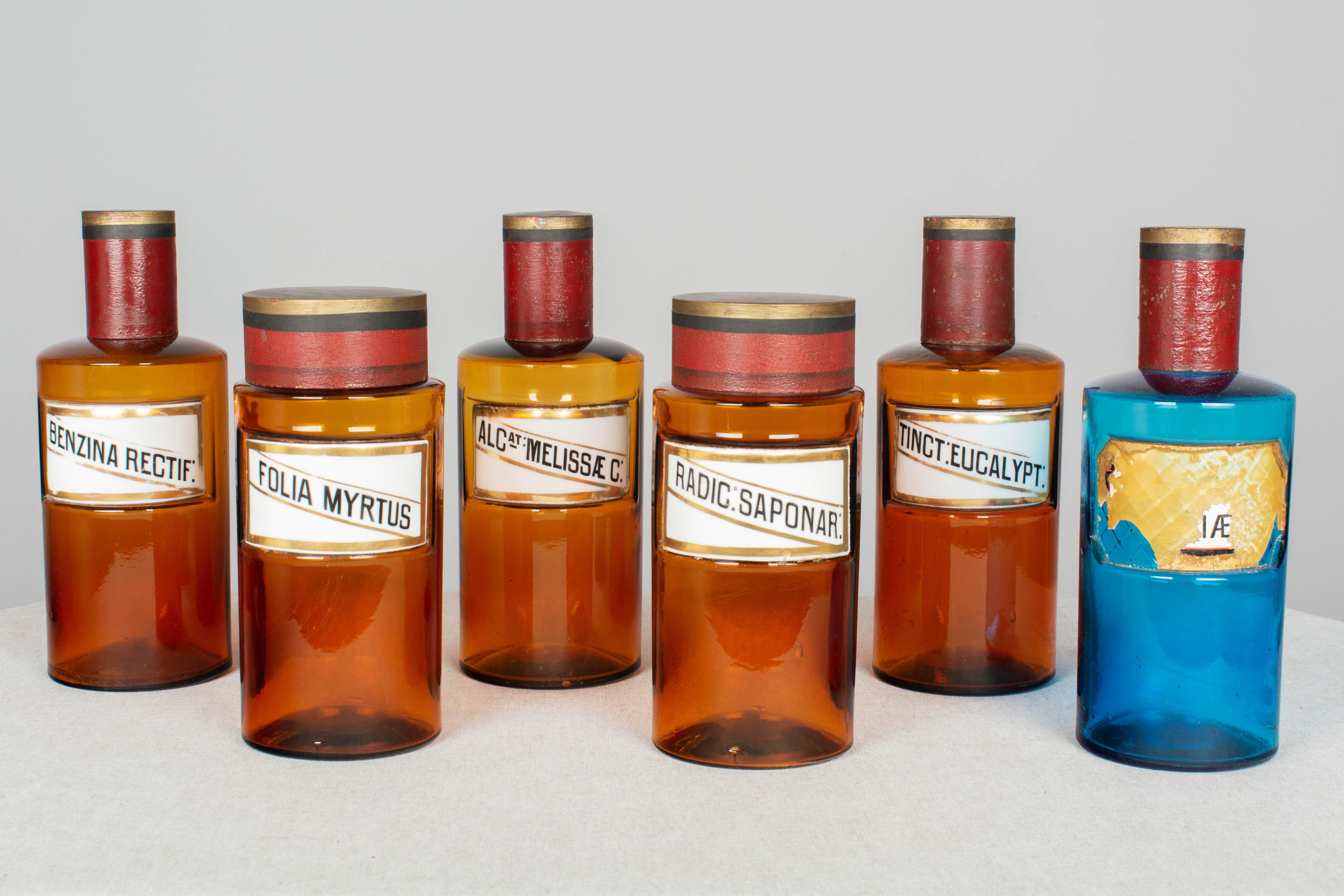 A set of five 19th century French glass apothecary jars with porcelain labels and painted tin lids. Five amber glass and one blue glass (with remnants of label). The neck of the 