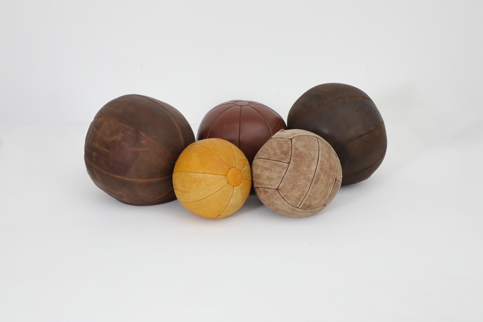 Set of five 1950's leather gymnastic medicine balls in assorted sizes and leather tones. Each ball has original leather with visible wear and patina, and repairs made to the stitching. Approximate diameters and weights are as follows: 8