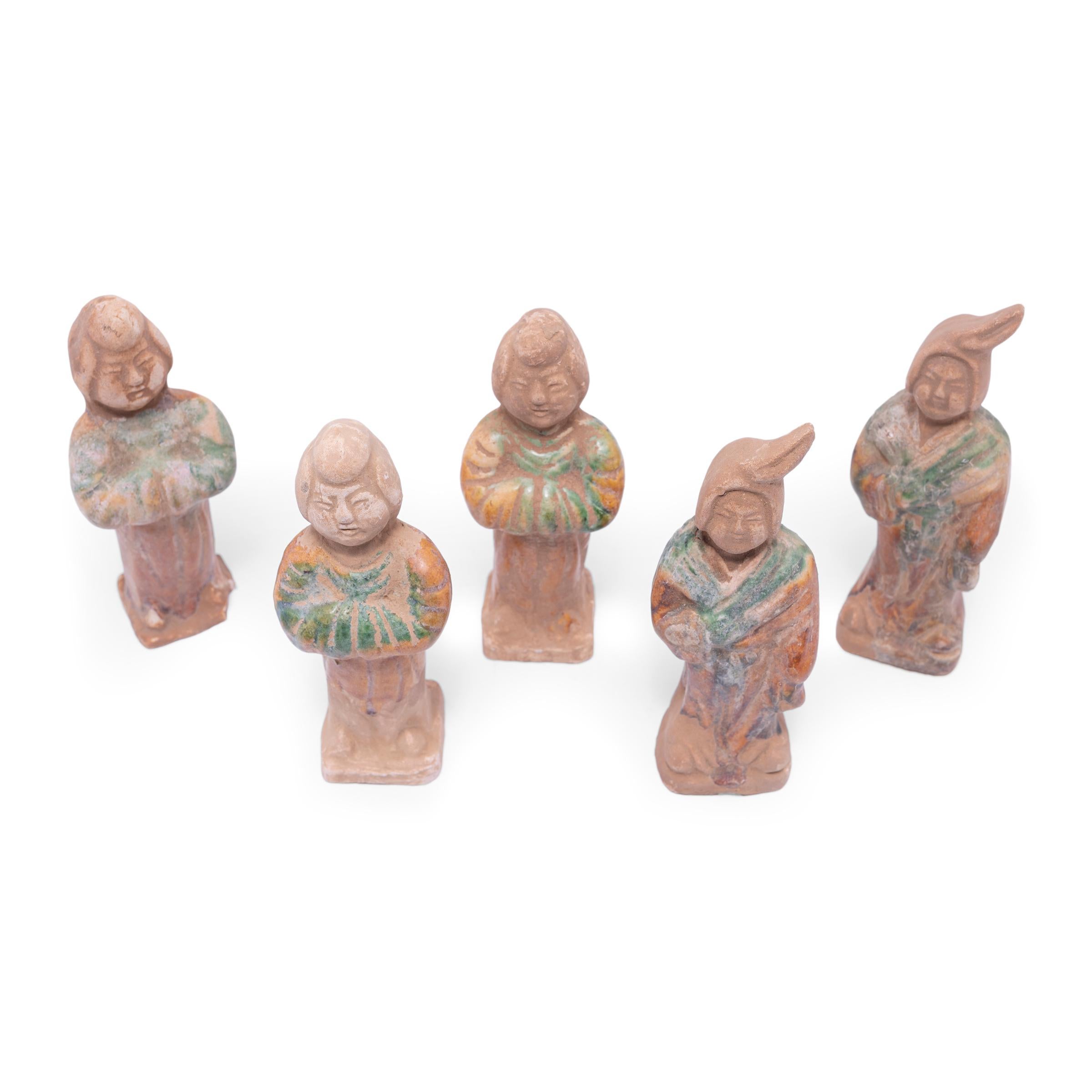 Molded of earthenware, this set of five petite sculptures are a type of centuries-old burial figurine known as míngqì. Such model figures were placed in tombs of individuals with high status to ensure a safe journey to the afterlife. Meant to depict