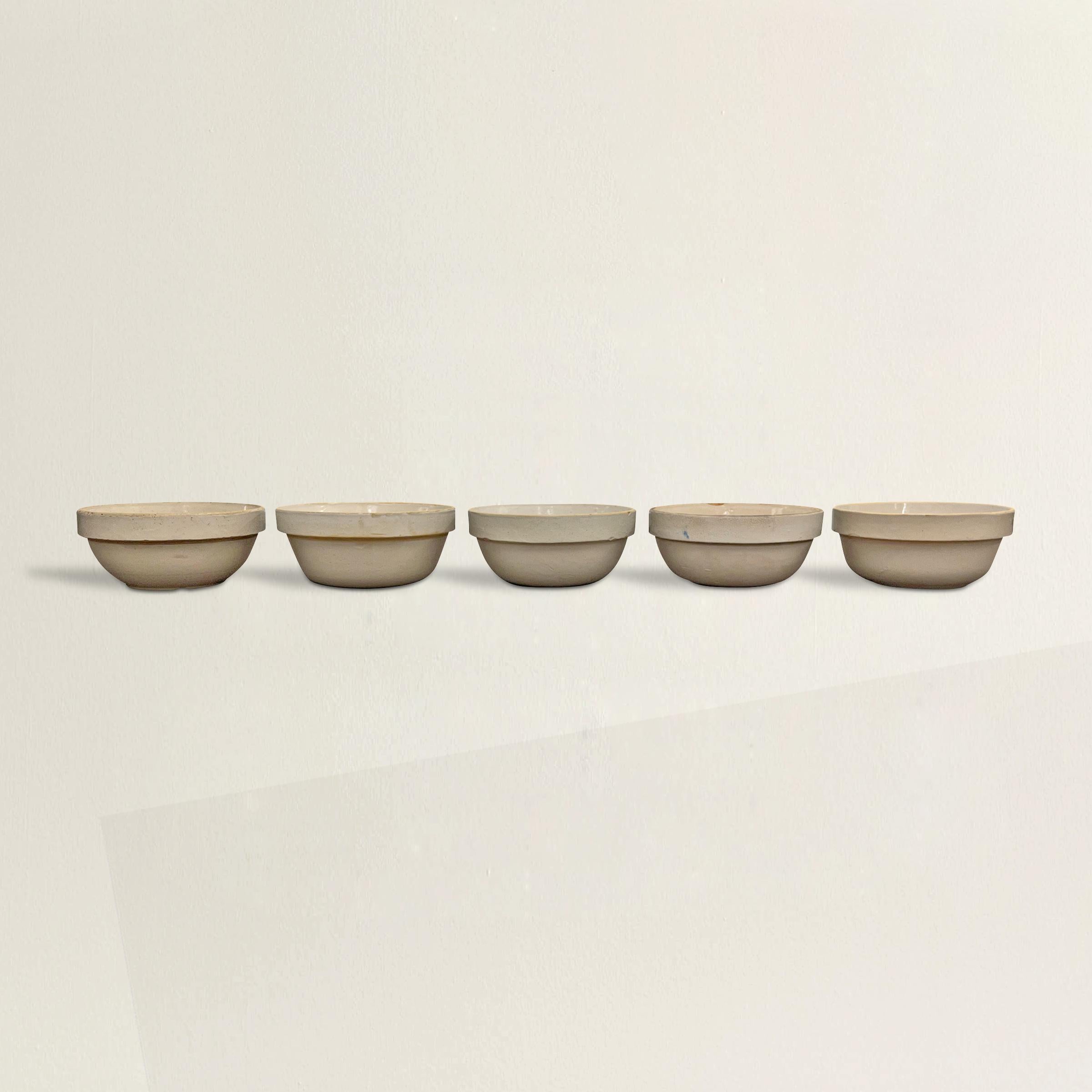 A charming assembled set of five early 20th century American zinc-glazed stoneware mixing bowls of simple, but sophisticated, forms and a blend of similar cream colors. Perfect for displaying on your kitchen shelves, lined up on your counters, or