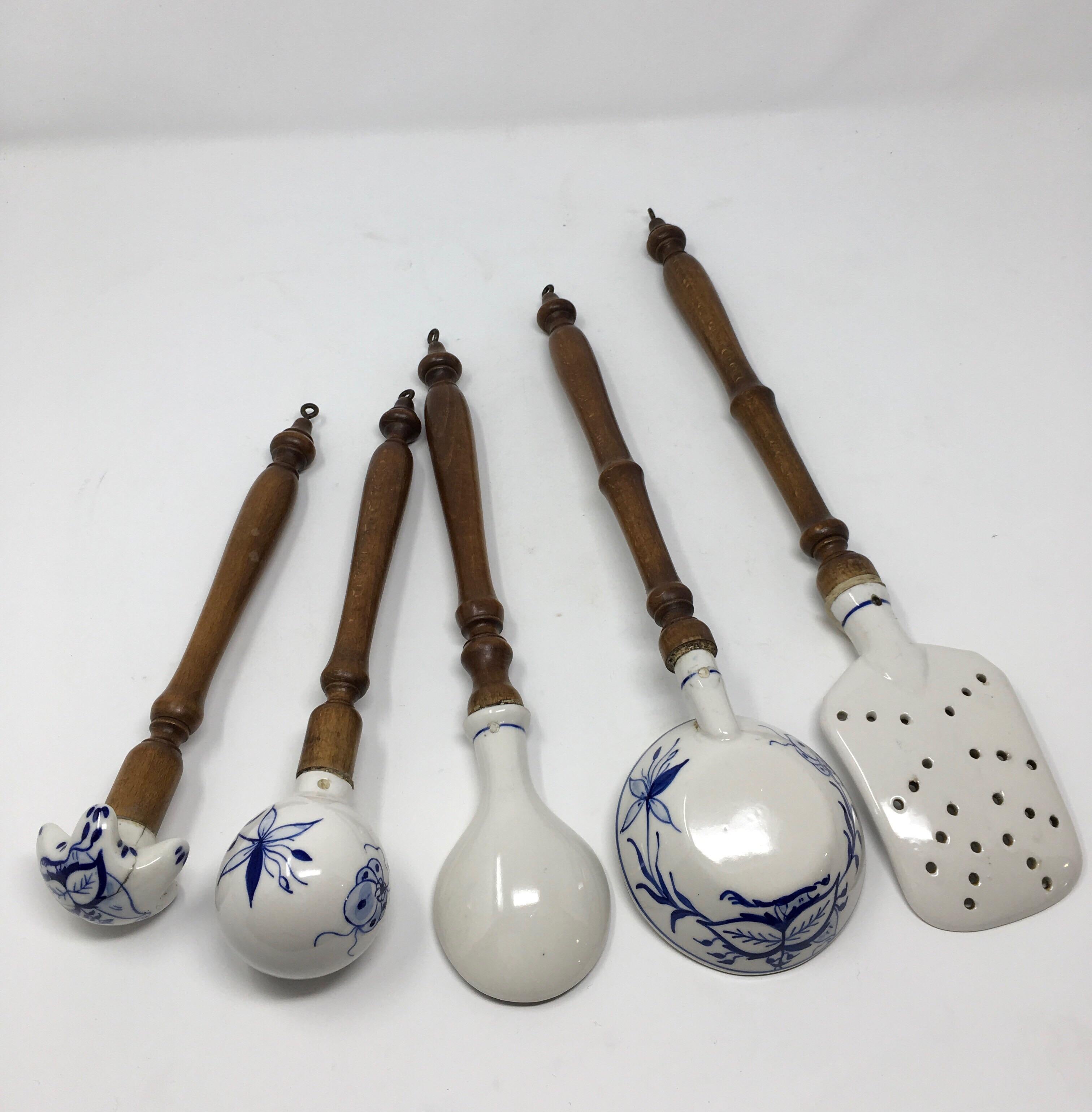 This is an antique set of five German blue and white porcelain kitchen utensils with turned wood handles. The wood handles have small metal hooks to hang and display the pieces. These pieces have been well used and loved, some pieces have chips and