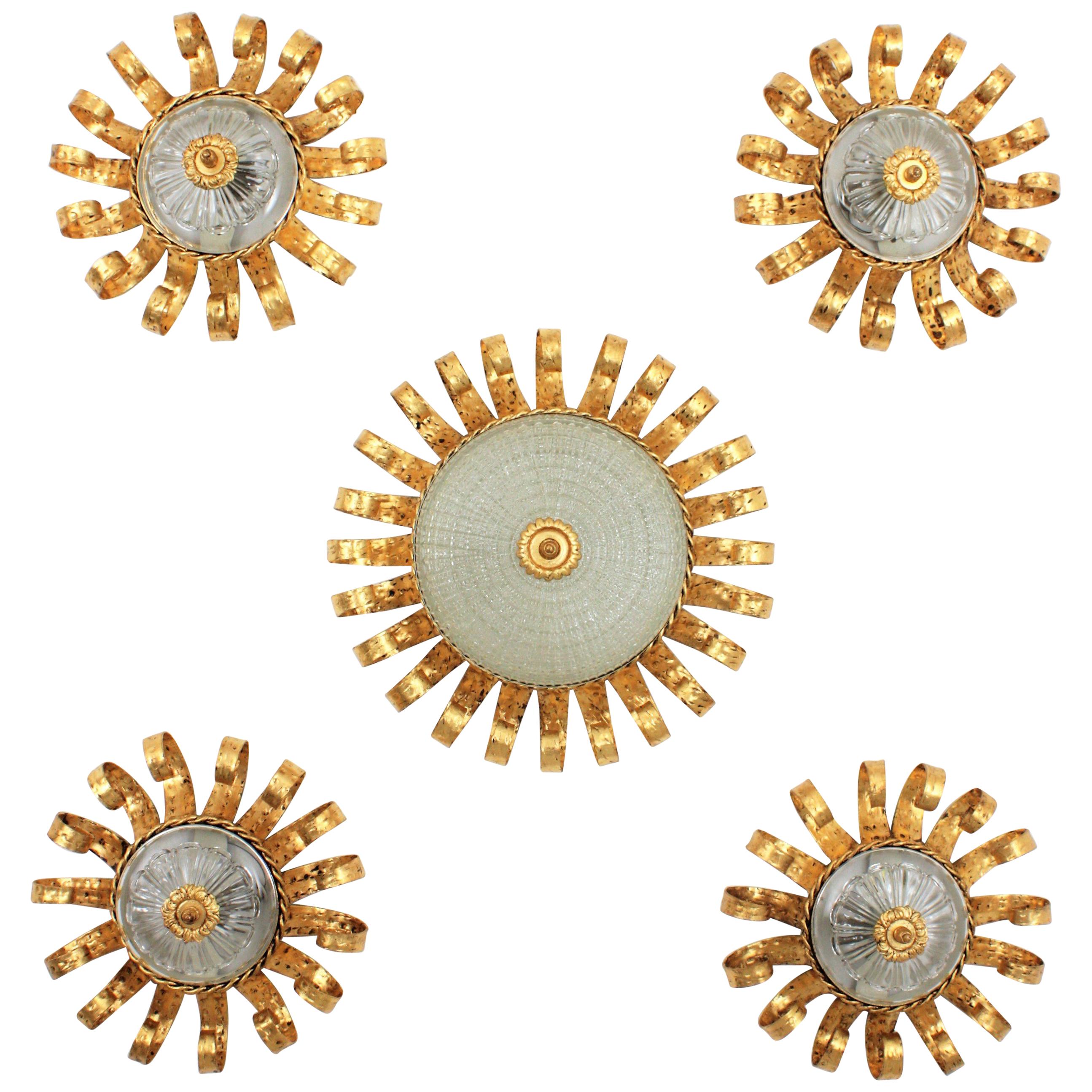 A magnificent set of Brutalist hand-hammered iron sunburst crown light fixtures with scrolled frames, central glass difussors and gold leaf finish.
Spain, 1960s.
The set is composed by 4 small flush mounts and a larger one. The hand-hammered work