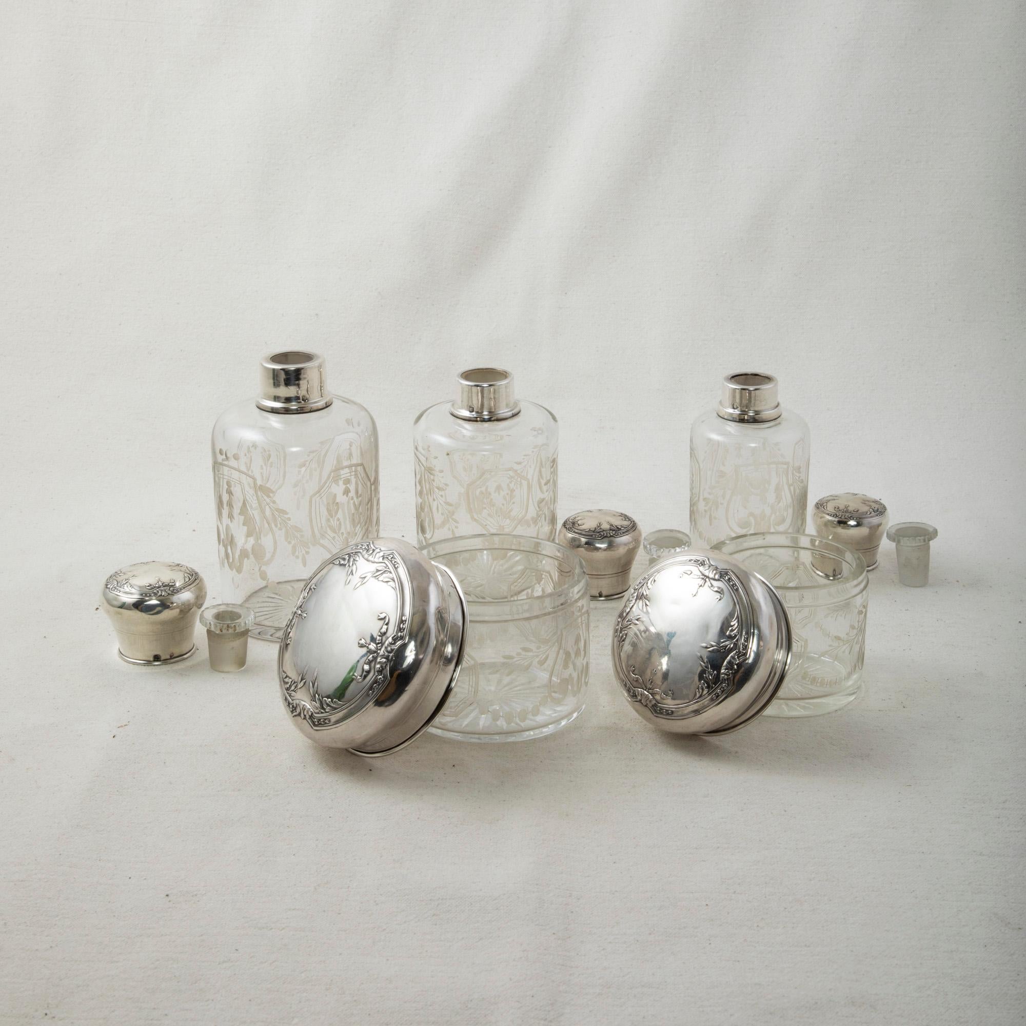 This set of five late nineteenth century French vanity bottles features an etched leaf pattern on the bottles and jars and sterling silver lids. The lids are detailed with classic Louis XVI motifs including ribbons and laurels. Each lid is stamped