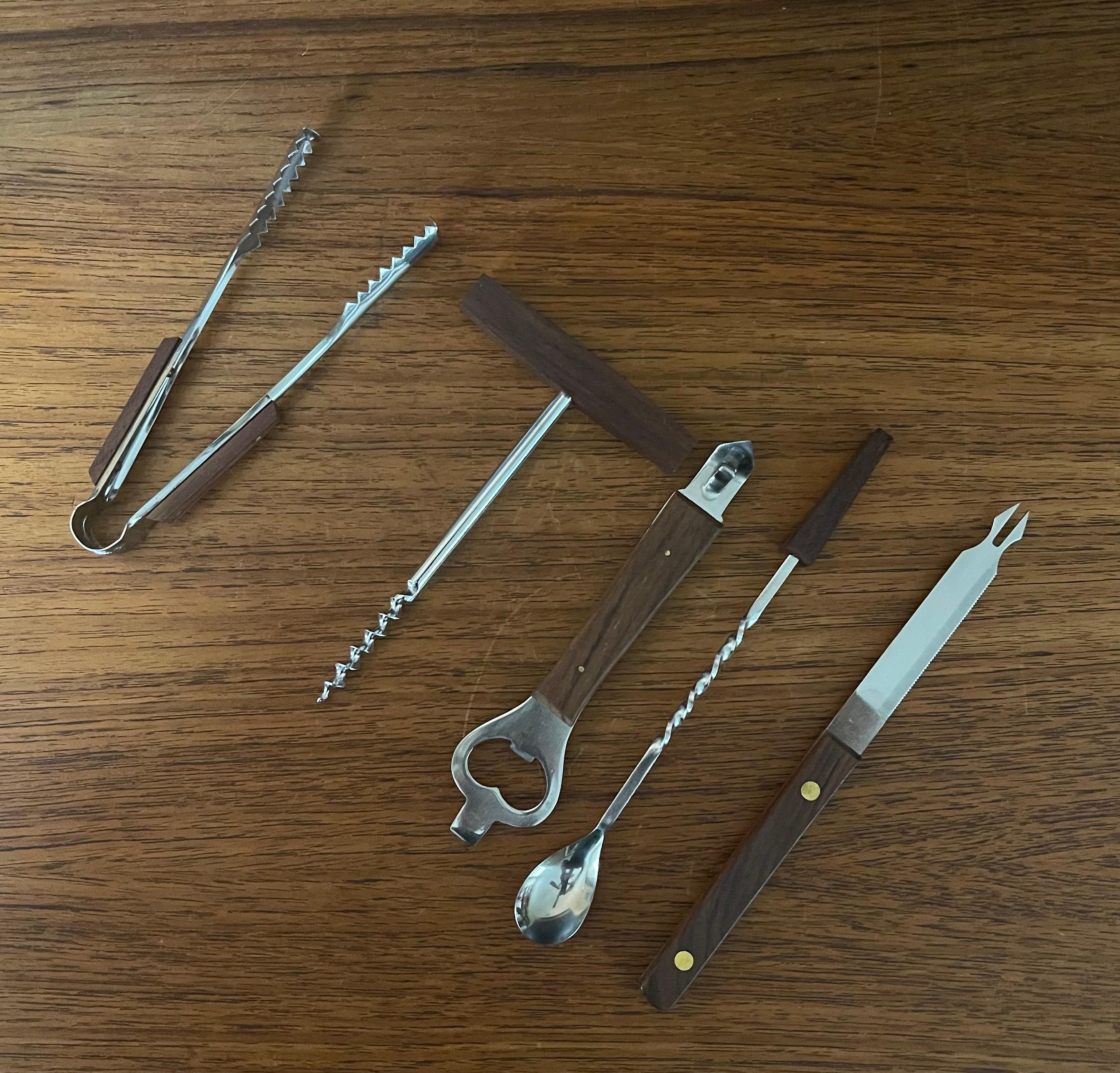 Set of five MCM walnut & stainless steel barware tools, circa 1970s. The set includes a bottle/ can opener, wine cork screw, ice tongs, stir stick and a citrus knife all made of stainless steel with walnut. The tools are in very good condition and