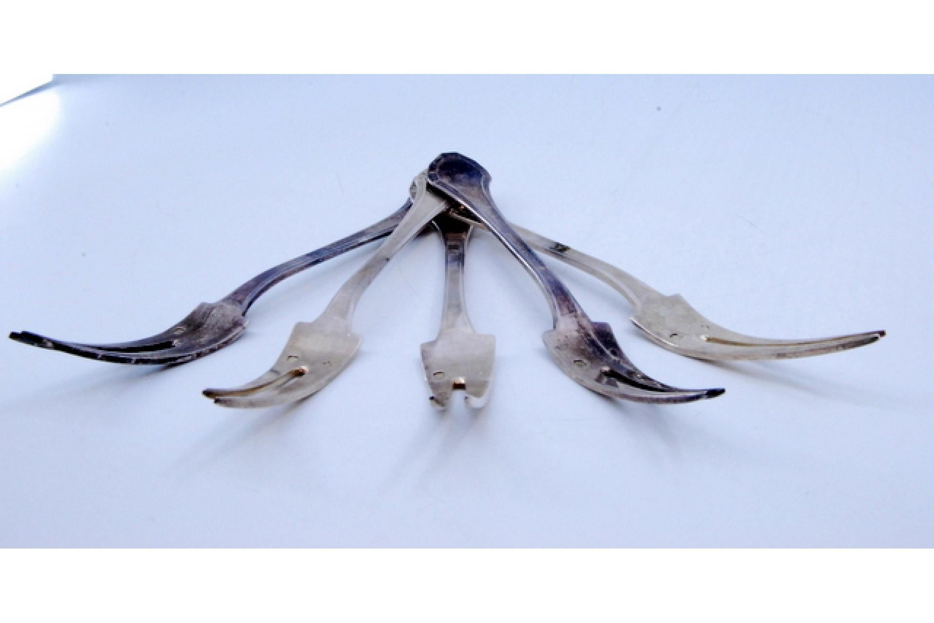 Descripción: Juego de cinco tenedores para pepinillos de plata con asas en relieve. Metal: Silver. Origen: Francés. Marca: Tête Minerve. Peso: 123,08 gramos. Dimensiones: 14.5x1.8. Contenido: 950/1000. Marca de ensayo: Sí, desde 1838. Información