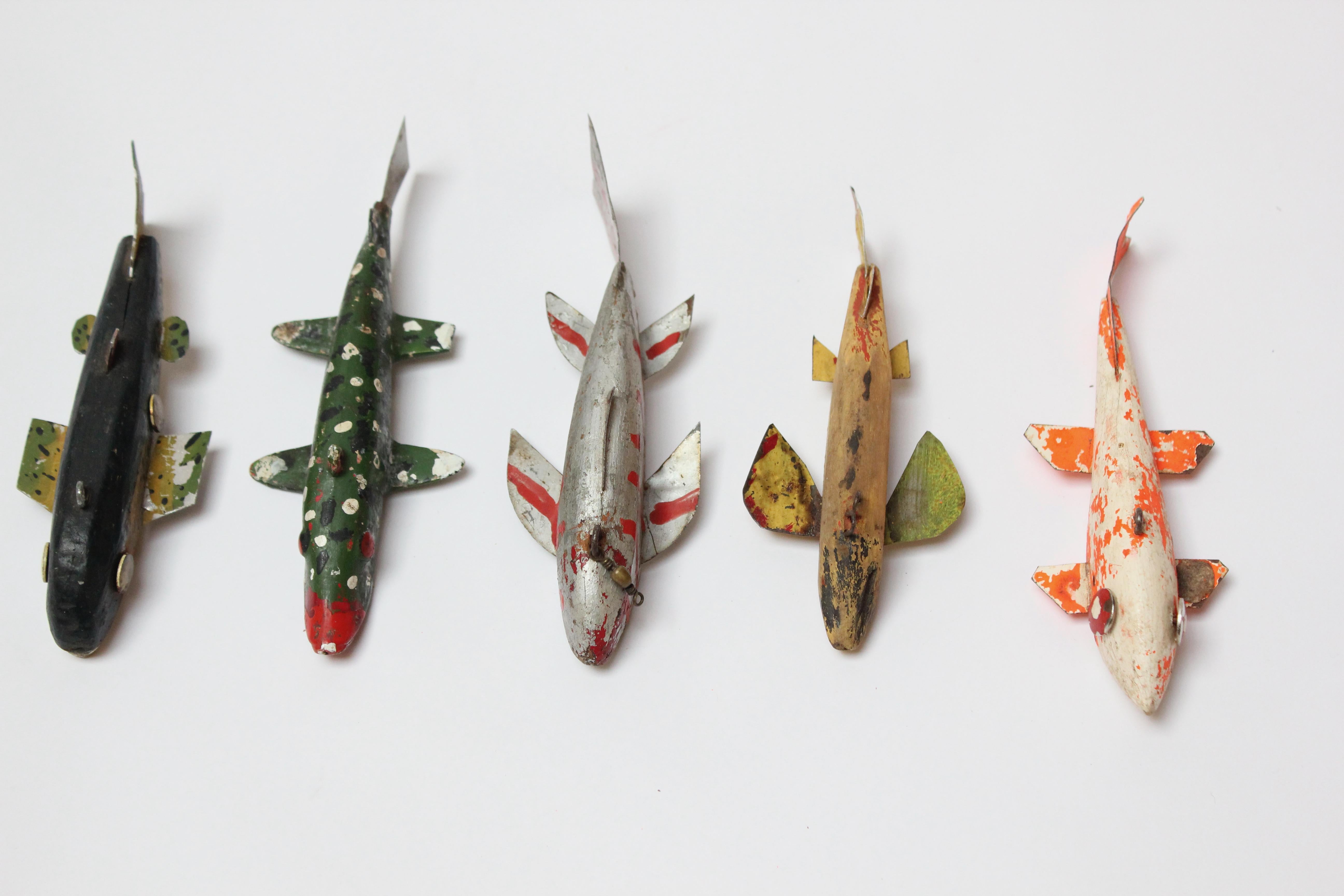 Group of five Folk Art fish decoys composed of painted tinned iron sheet metal or aluminum fins and tails and carved wooden weighted lead bodies, some with applied eyes; others with painted (ca. 1940s-1950, USA). 
Though all parts are intact (fins,