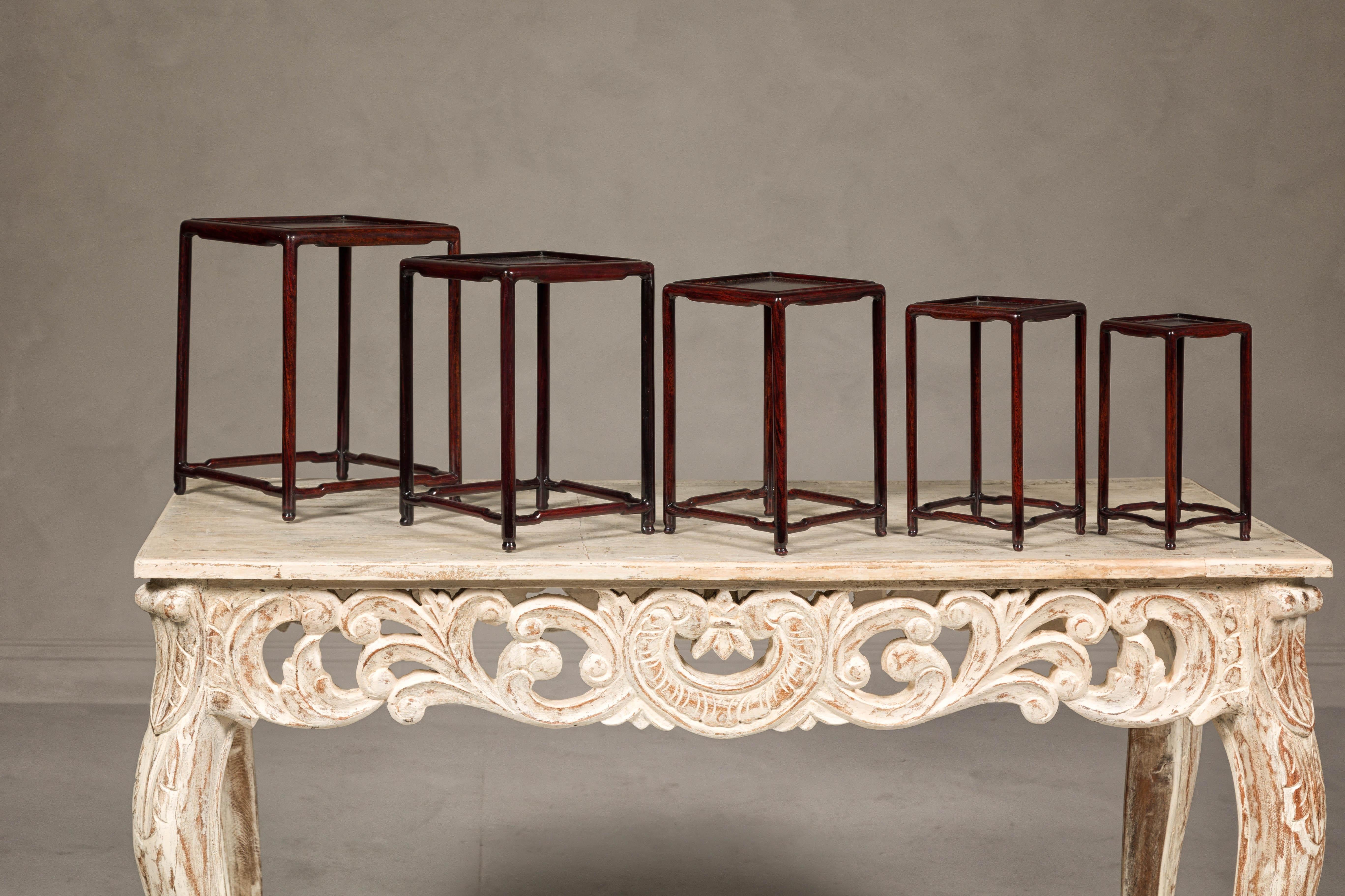 A set of five small size rosewood nesting tables with square inset tops, low humpback stretchers and reddish brown color. This set of five rosewood nesting tables from the mid-20th century exudes timeless elegance and sophisticated craftsmanship.