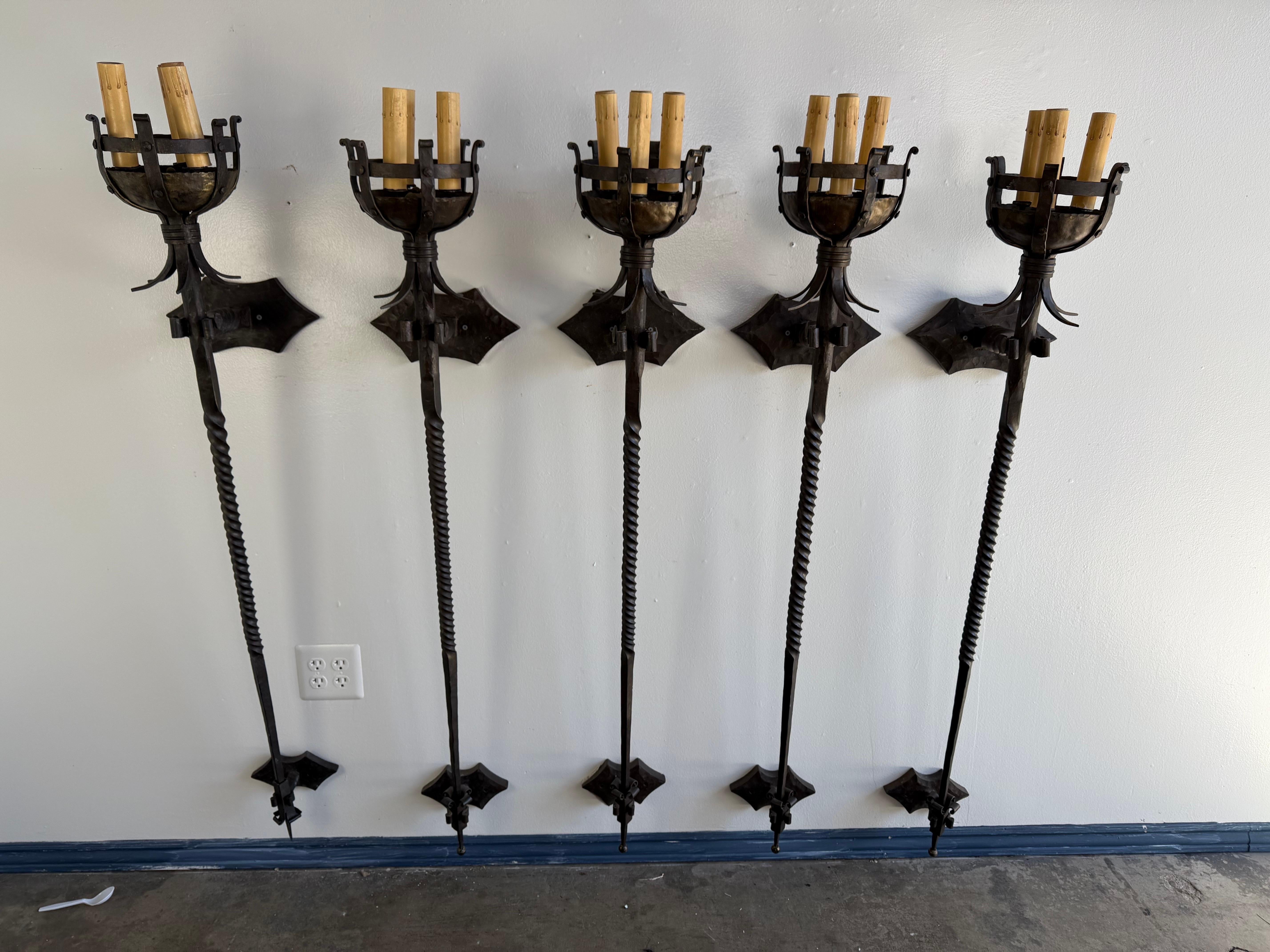 This striking set of five vintage wrought iron sconces comes from a historic landmark home in Hancock Park, a neighborhood known for its grand architecture and early 20th-century estates. Each sconce features a tall, dramatic silhouette with a