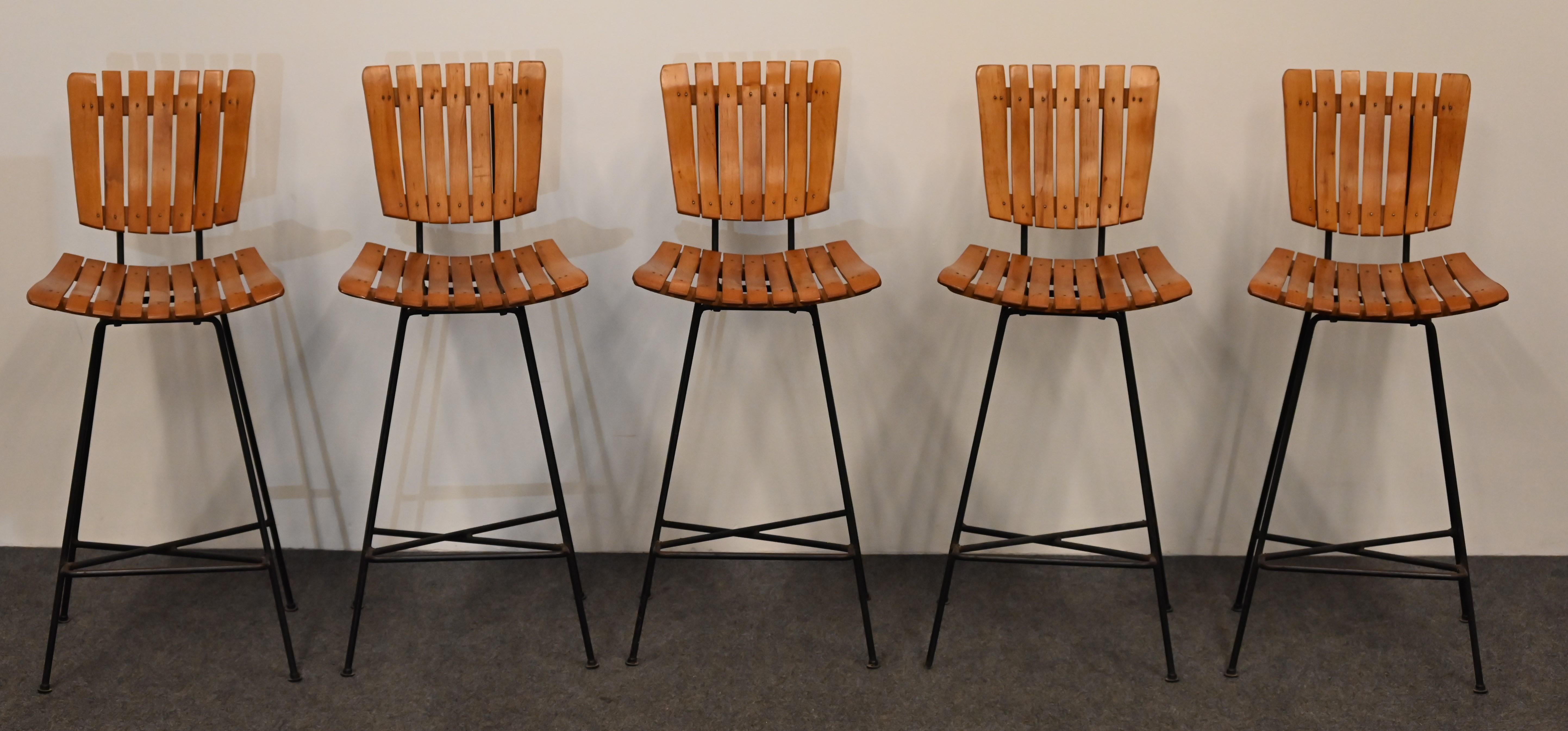 A mid-century set of five slatted maple wood and iron bar stools designed by Arthur Umanoff. This set of counter stools would look great in any modern, contemporary or traditional setting. The designer stools are in very good condition with