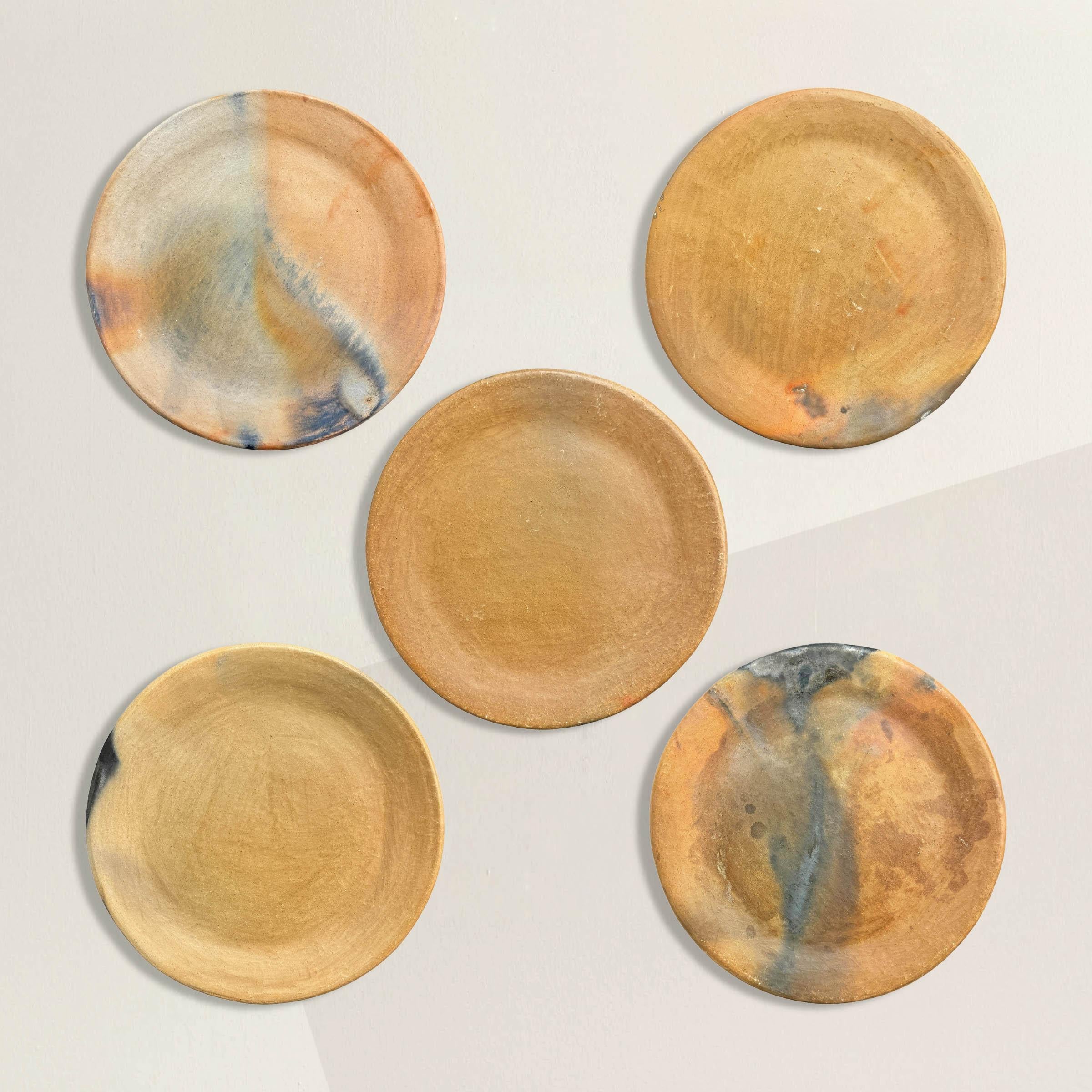 Elevate your culinary presentations and home decor with this set of five wood-fired terra cotta plates, each bearing a distinct pattern of burn and smoke marks, a testament to their artisanal craftsmanship. These plates not only serve as functional