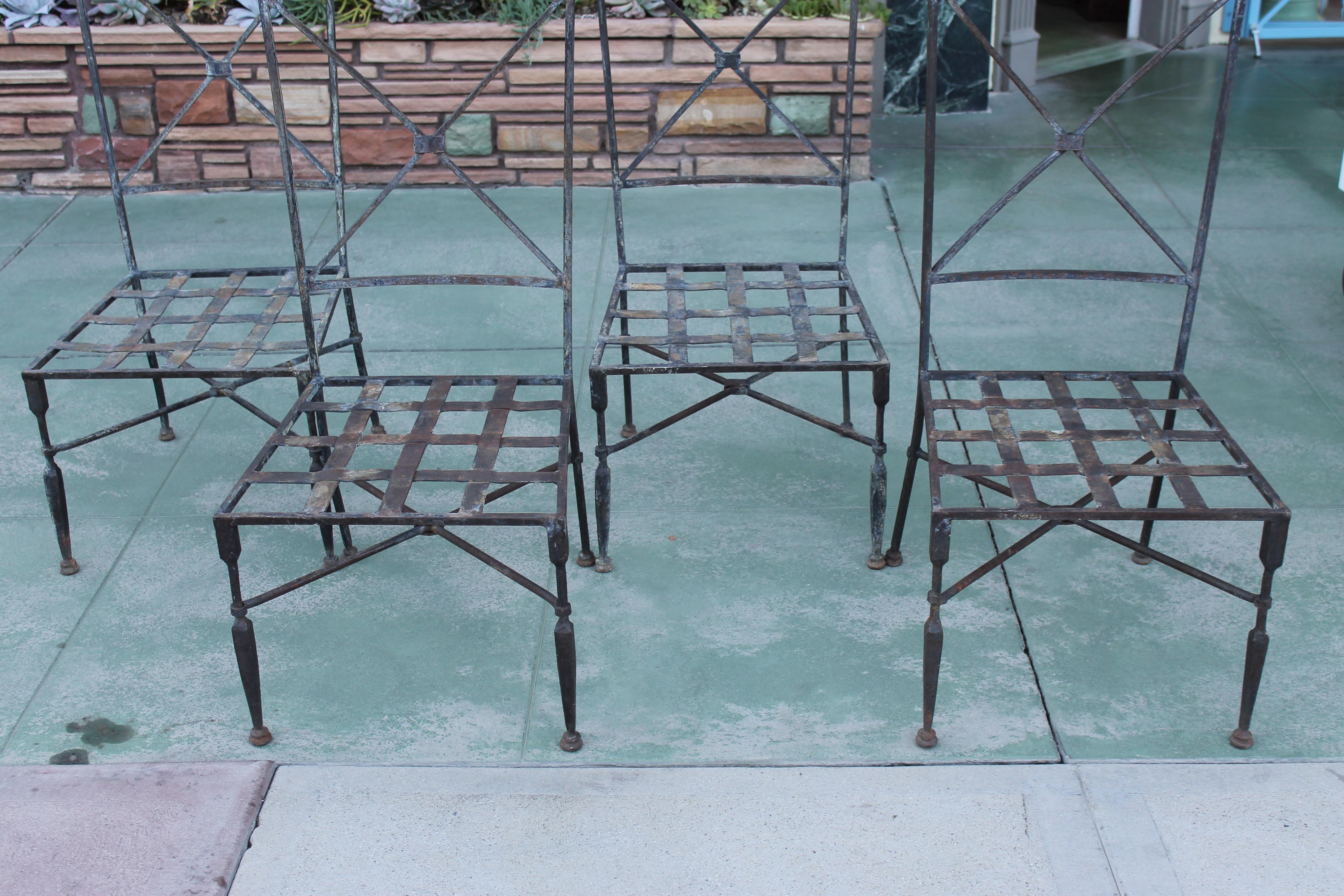A set of four handsome hand forged iron chairs in a neoclassical style. Lots of beautiful detail, including forged straps at the intersections of the cross bars and heavy basket weave seats. Front legs are especially good looking. Suitable for