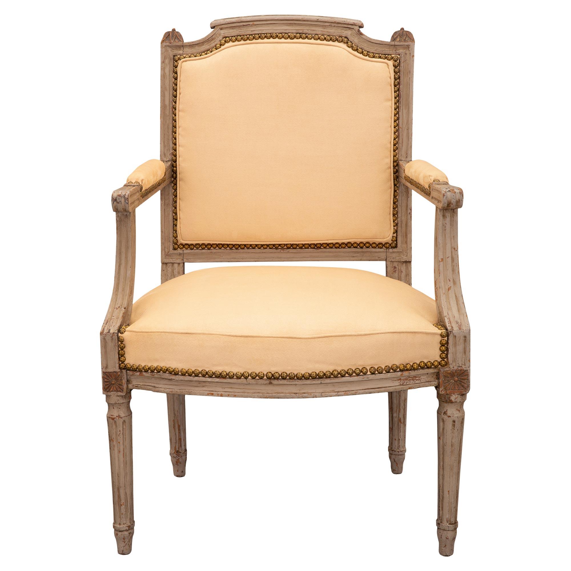 A charming set of four 18th century French Louis XVI period patinated arm chairs. Each with a rectangular upholstered backrest, the top rail is fluted and flanked by circular capital carved laurel leaves. The padded arm rests have fluted down swept