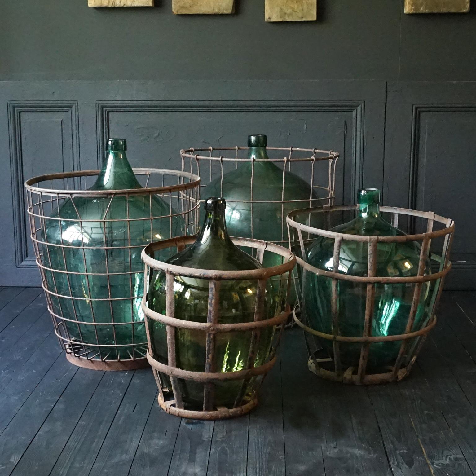 Very decorative set of 4 antique green hand blown and glass bottles also known as Demijohn, Lady Jeanne, Dame Jeanne or Carboy. 
Bottles like this were primarily used to hold liquids such as wine, cognac or brandy.
The metal baskets were to
